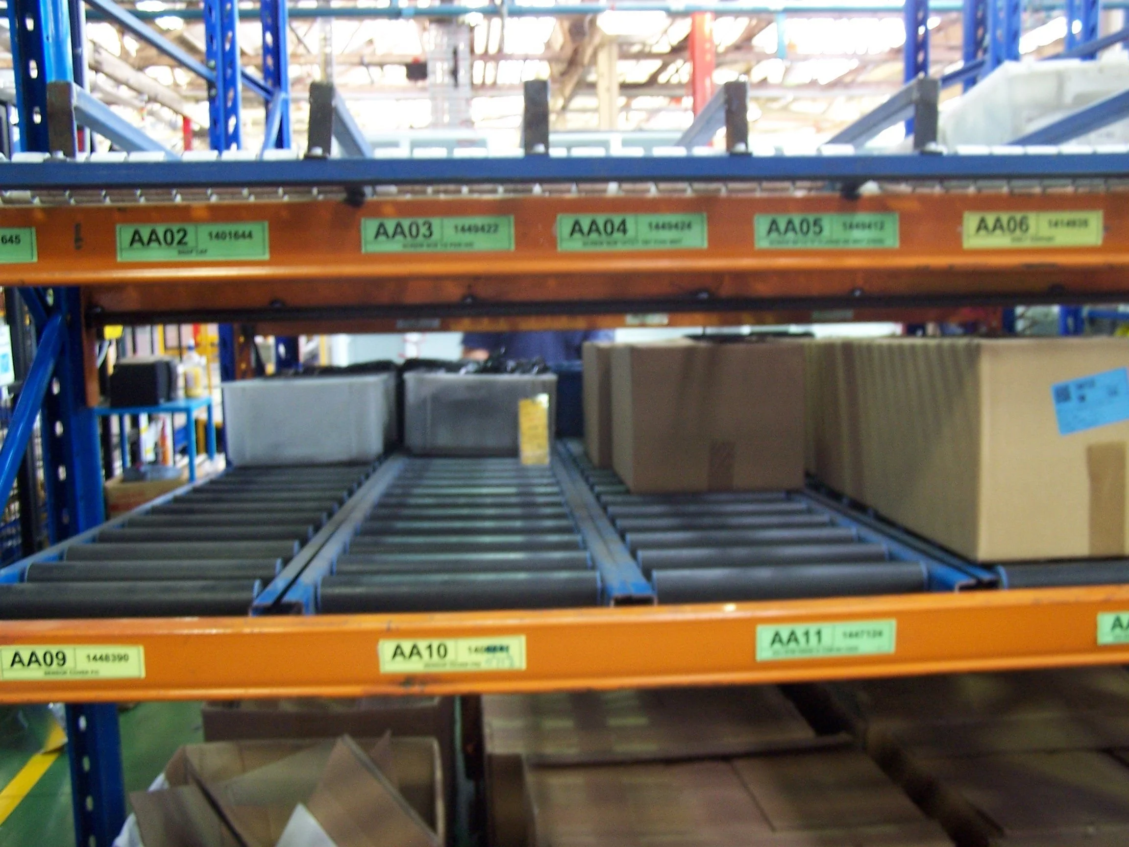 Empty store shelving unit in a warehouse with green labels and some boxes on the lower shelves.