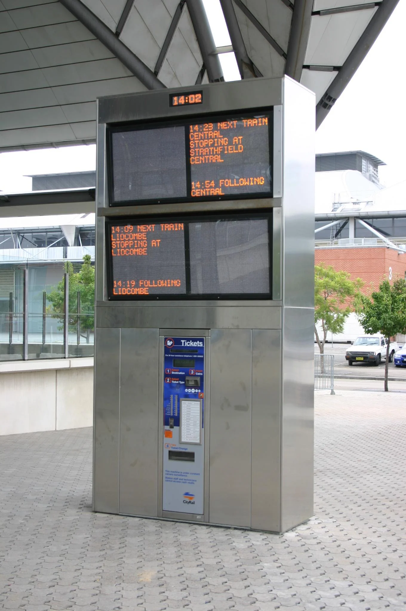 A digital train timetable display showing upcoming trains at a train station, with the current time 14:02, and details about trains scheduled to arrive at Lidcombe and Central stations.