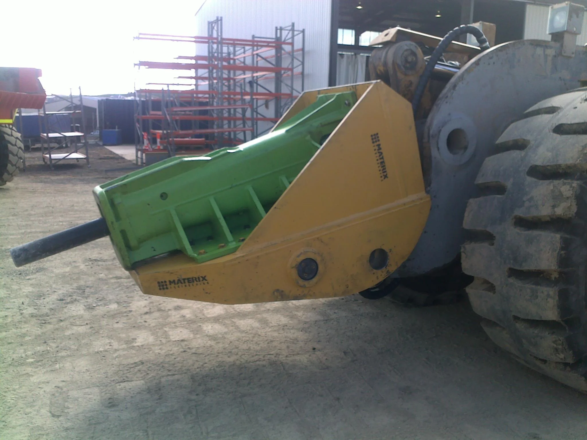 Close-up of a yellow and green attachments on a large construction vehicle in an outdoor construction site.