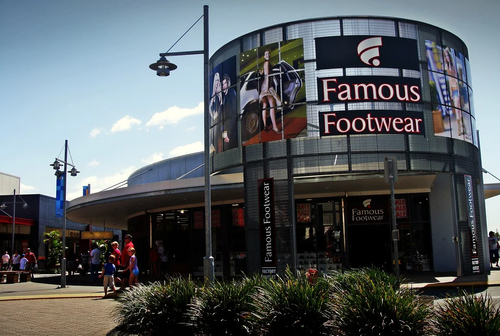 Famous Footwear store storefront with signage and digital billboard, busy shopping area, with pedestrians walking.