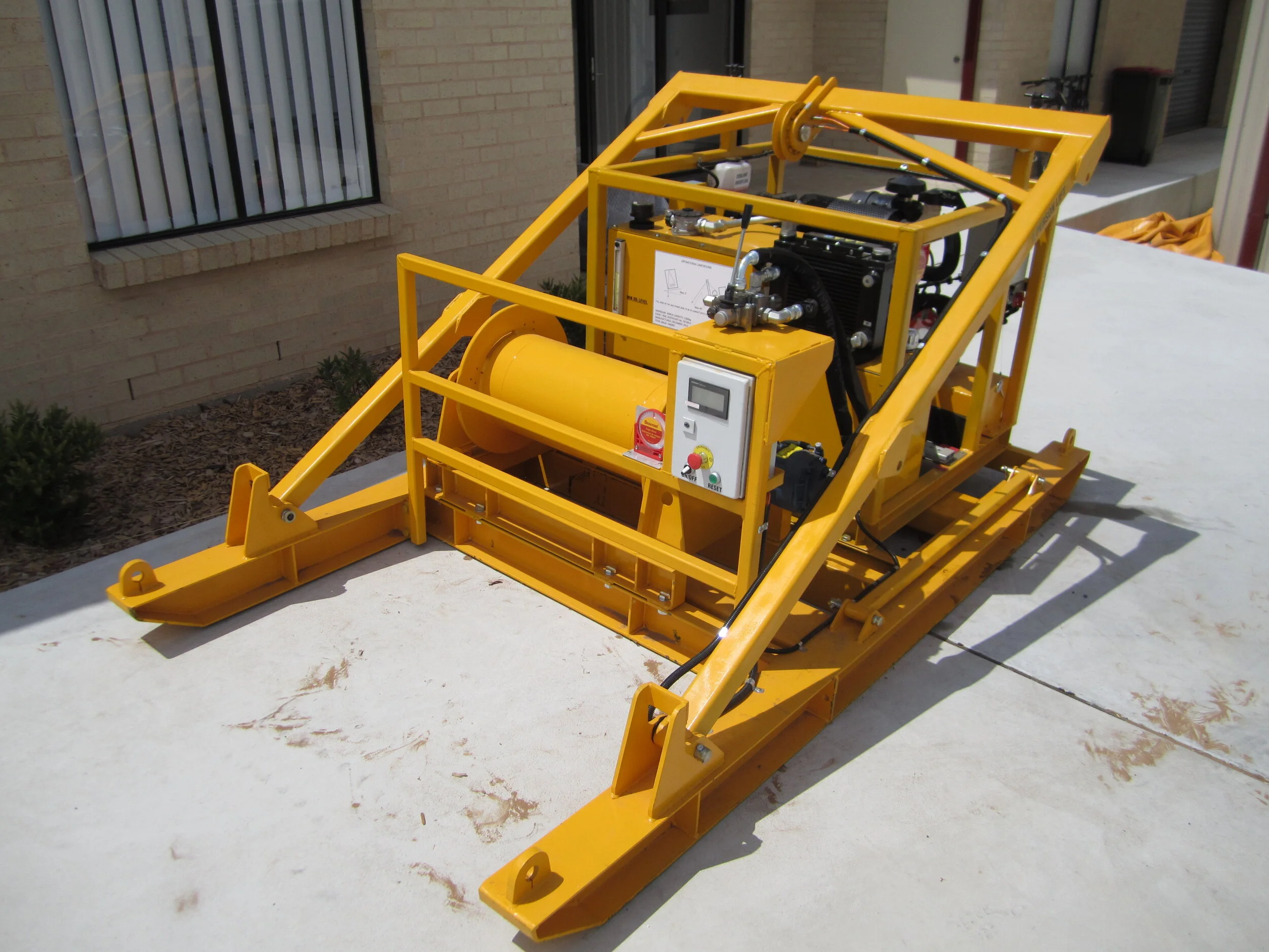 Yellow industrial machine with hydraulic components and control panel on a white surface outdoors.