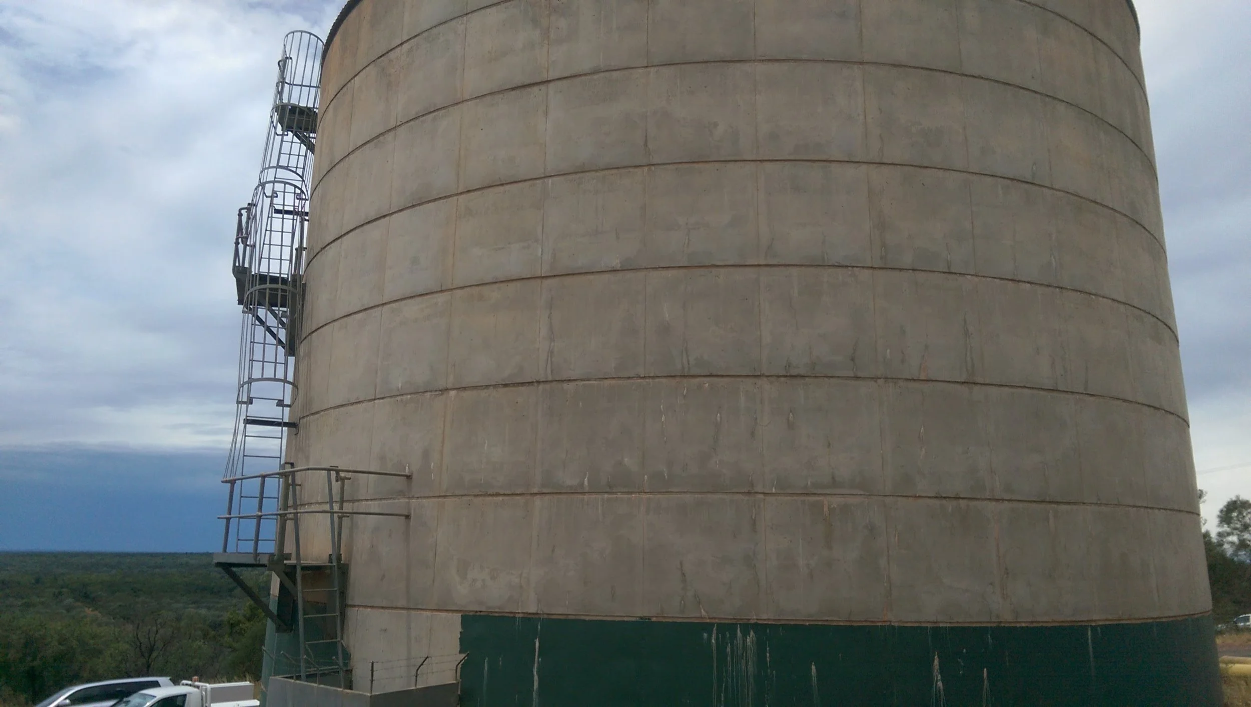 A large, beige concrete water tower with metal staircase and safety railing.