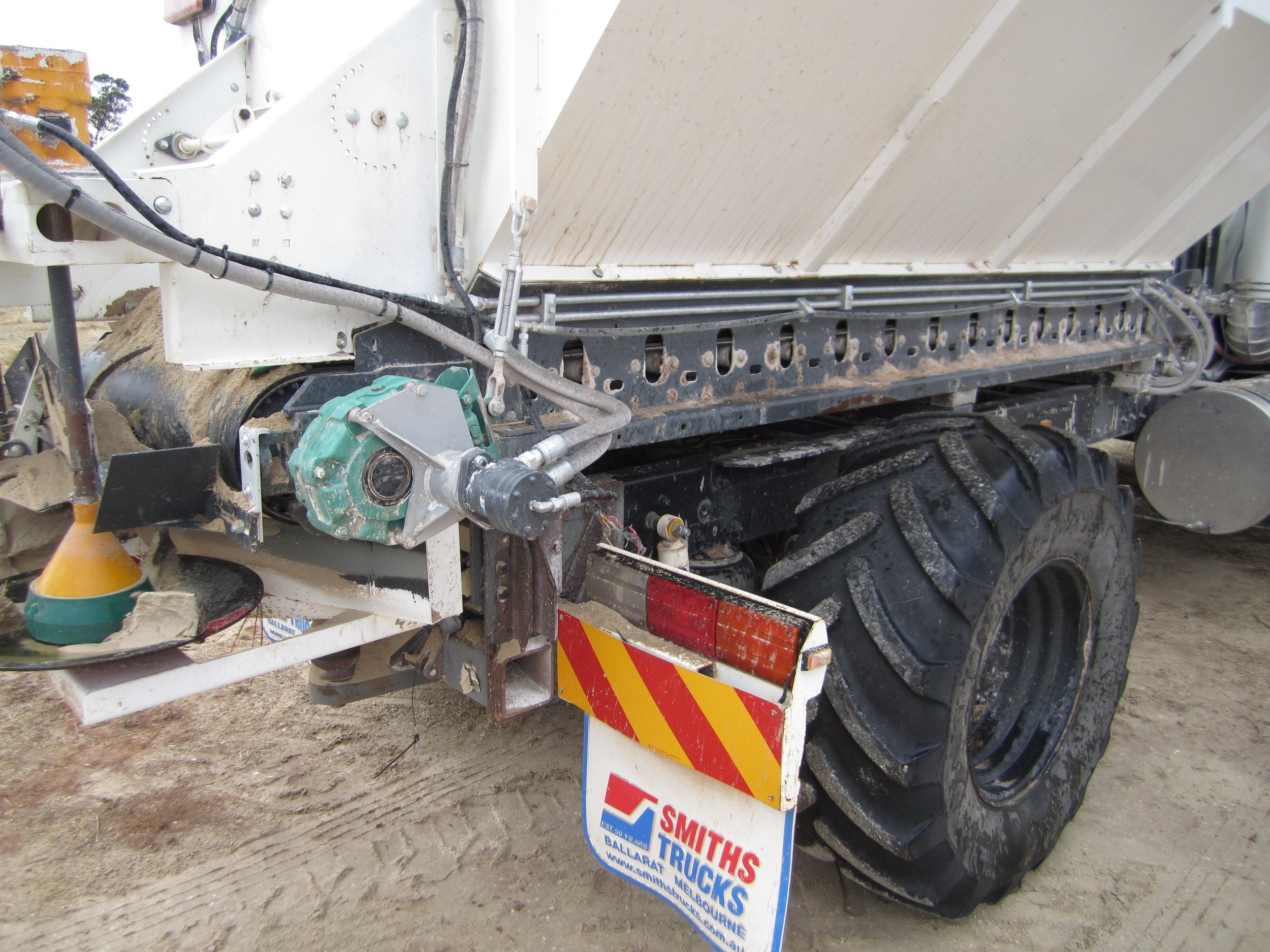 Close-up of a truck with construction equipment, showing hydraulic hoses, a green motor, and a sign that reads 'Smiths TrucKs' attached to the vehicle.