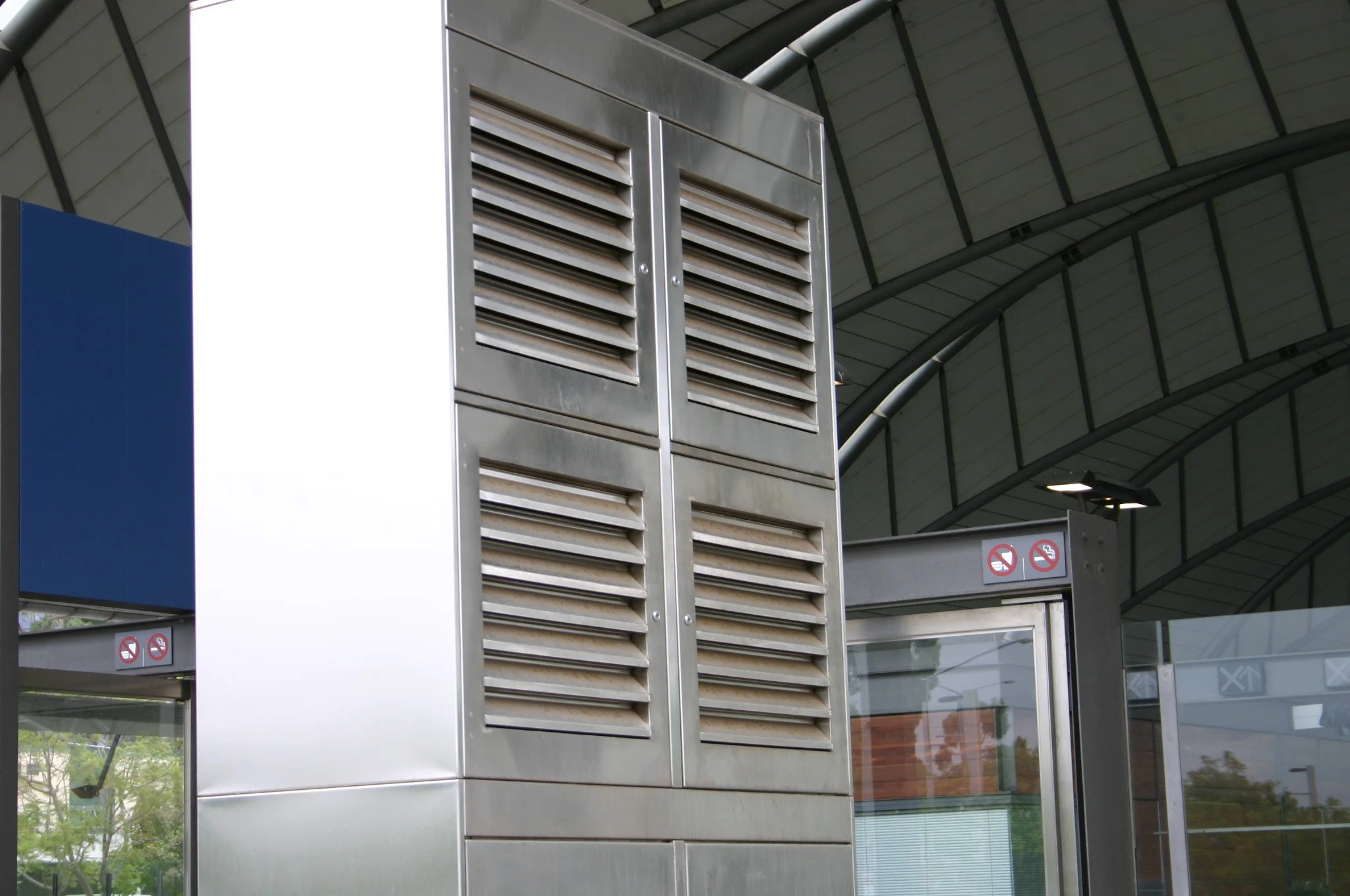 A stainless steel air vent or grille structure at an airport or modern building entrance with no smoking signs.