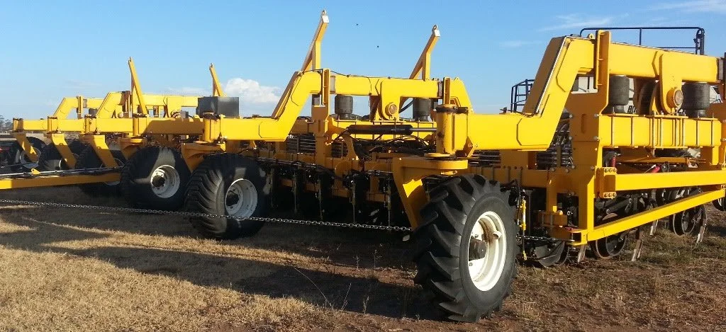 A large yellow farm implement with multiple sections and big black tires, set on a grassy field under a blue sky.