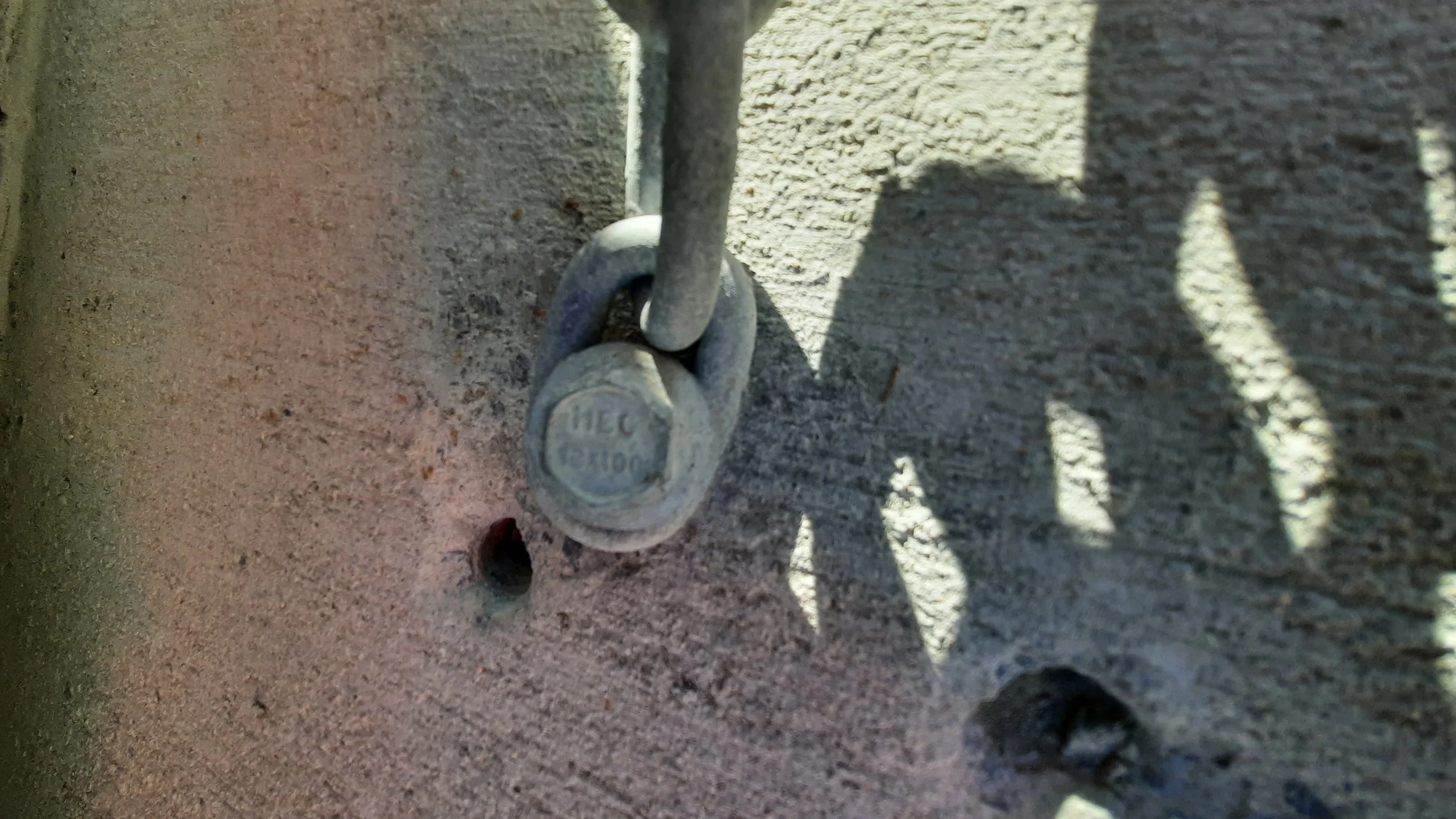 Close-up of a metal anchoring device attached to a concrete surface, with a shadow cast on the right side.
