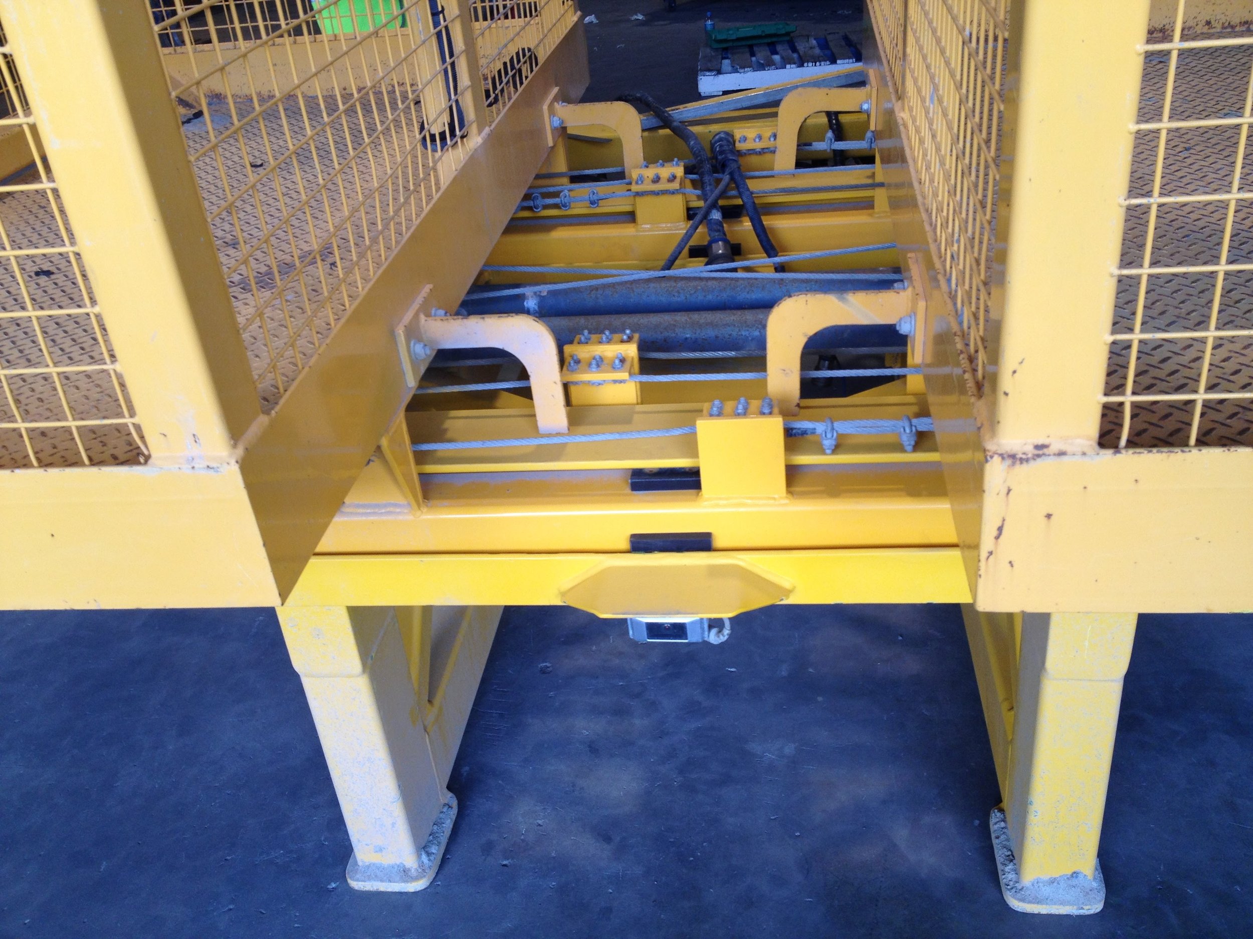 Close-up of a yellow metal construction or industrial equipment with hydraulic hoses and mechanical parts.