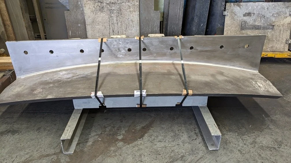 Large metal blade or scoop with a curved shape, mounted on a sturdy metal stand in an industrial workshop.