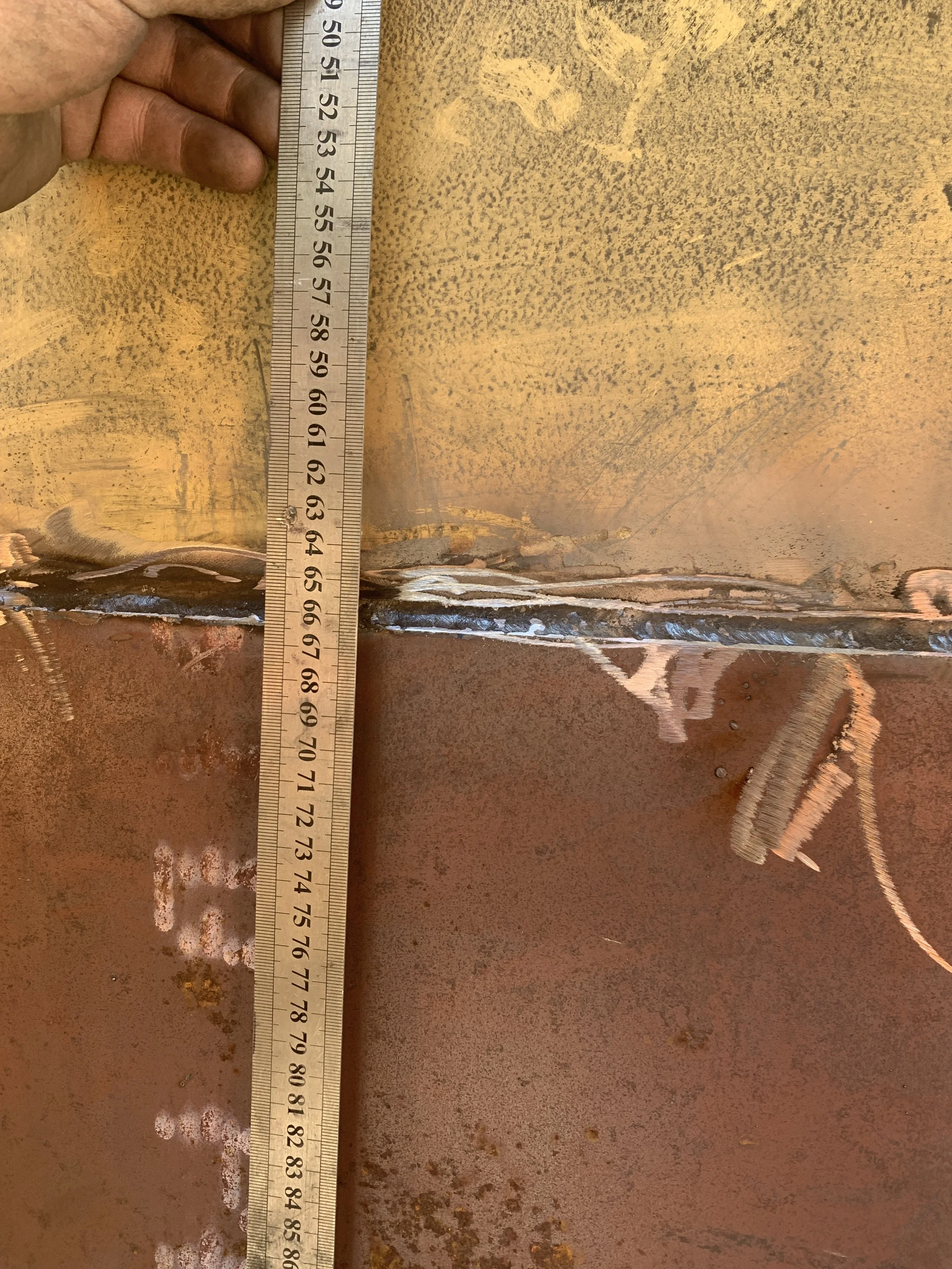 A person holding a metal ruler next to a piece of metal at least 21 inches in length