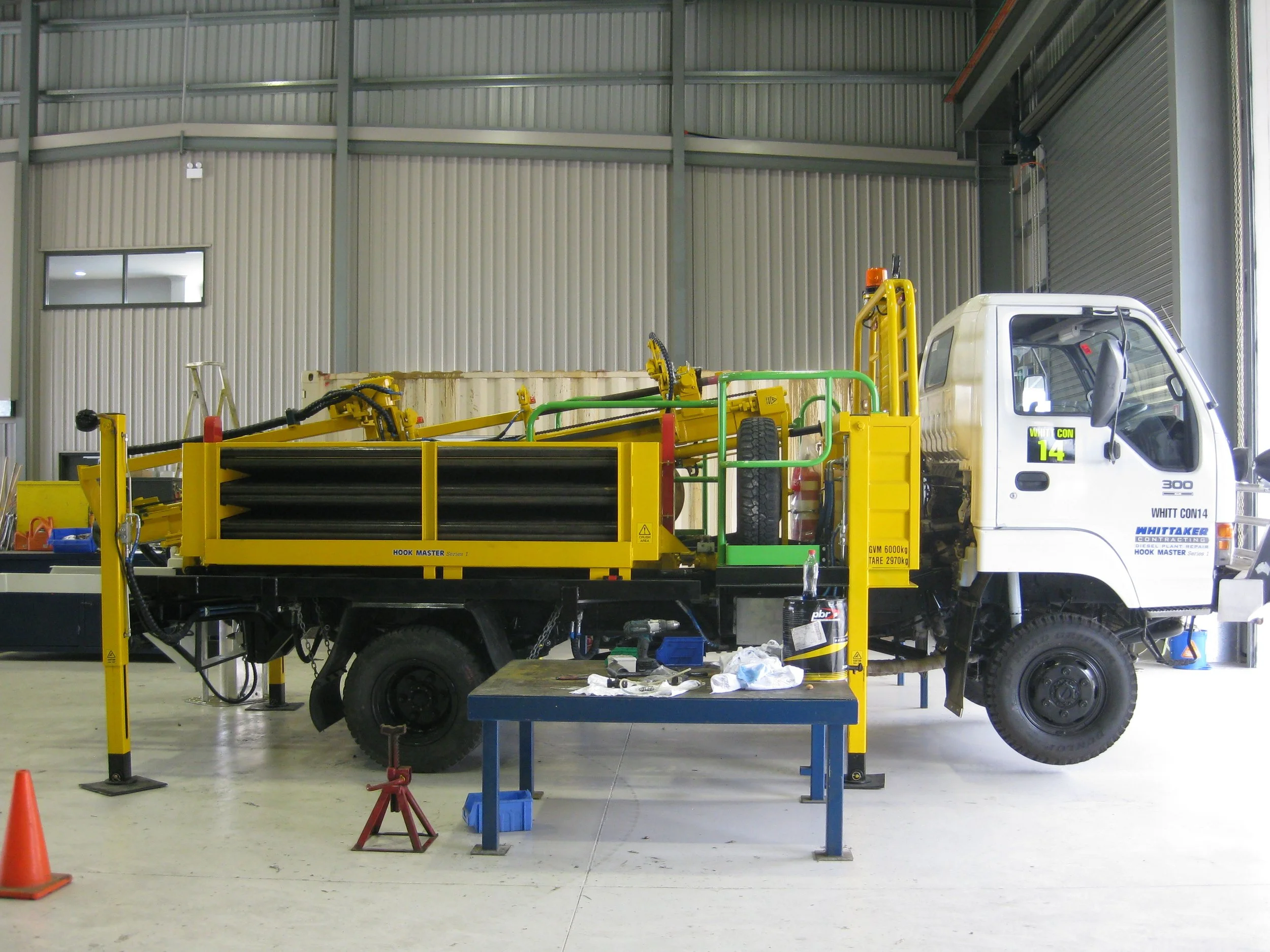 A white utility truck with yellow hydraulic equipment attached inside a large industrial warehouse.