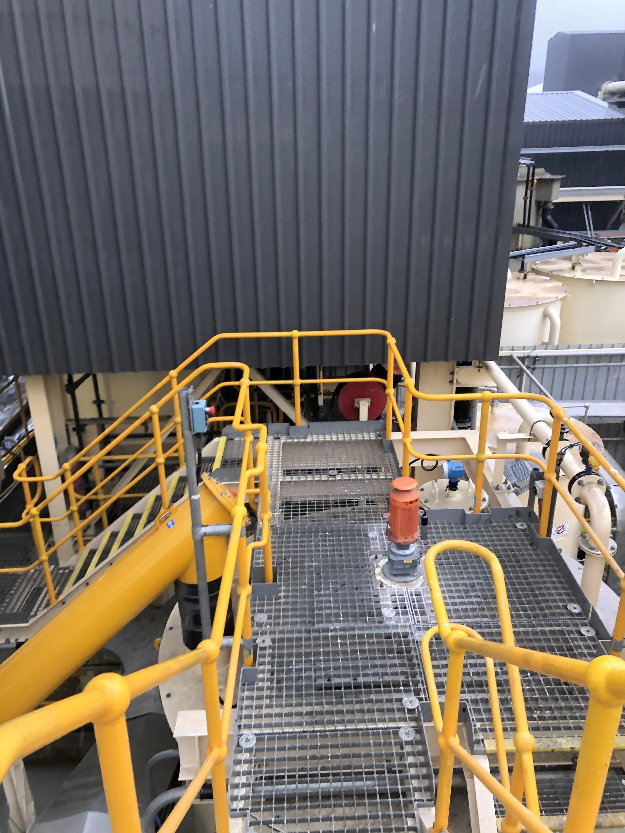 Industrial machinery with yellow safety railings, a grated metal platform, and pipes in a factory setting.