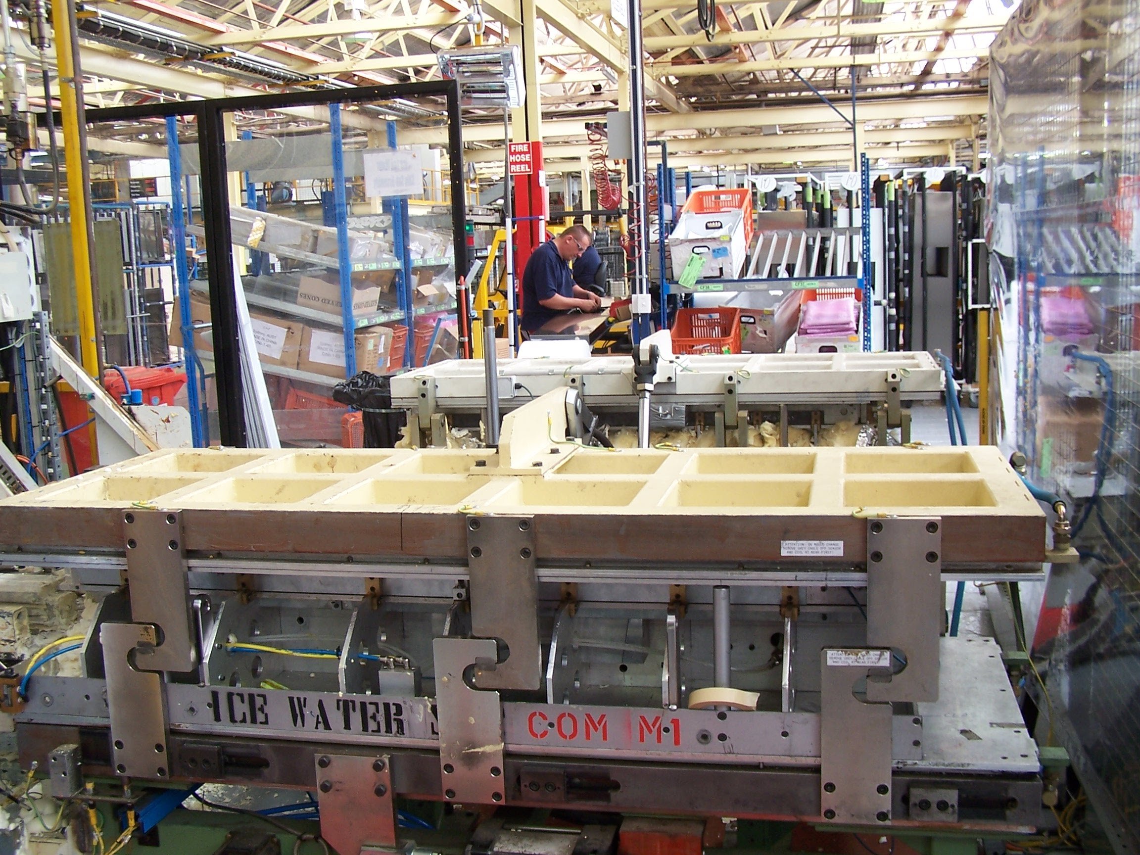 Close-up of an industrial machine with metal parts, wires, and a yellow frame, situated in a factory or warehouse setting.