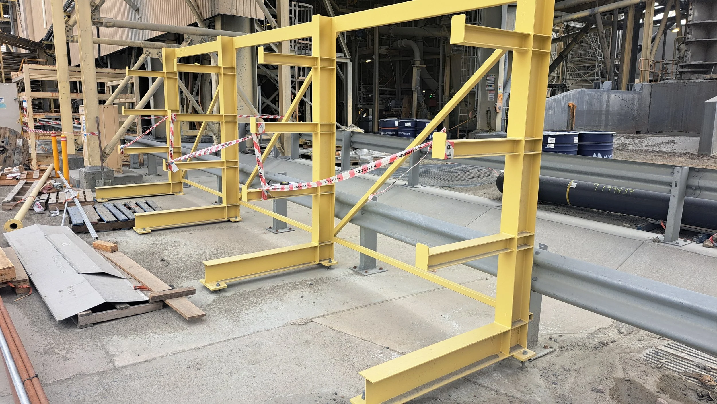 Construction site with yellow safety barriers, pipes, and scaffolding.