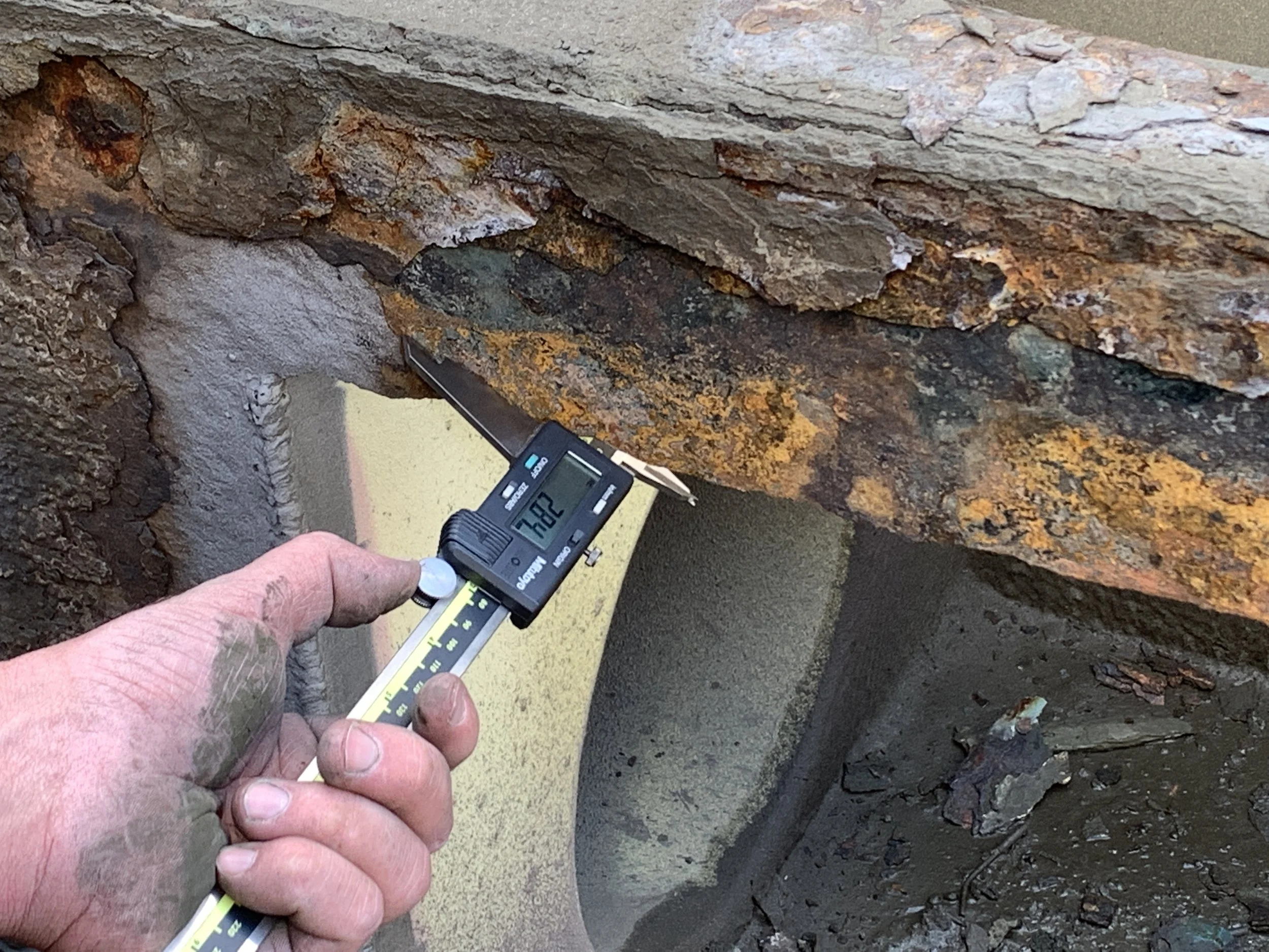 Close-up of a person's hand holding a digital measuring device against a rusty, layered rock surface.