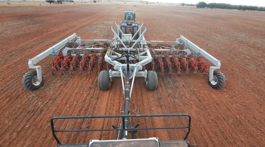 View from behind a tractor with a large seed planter attached, planting seeds on a red dirt field.