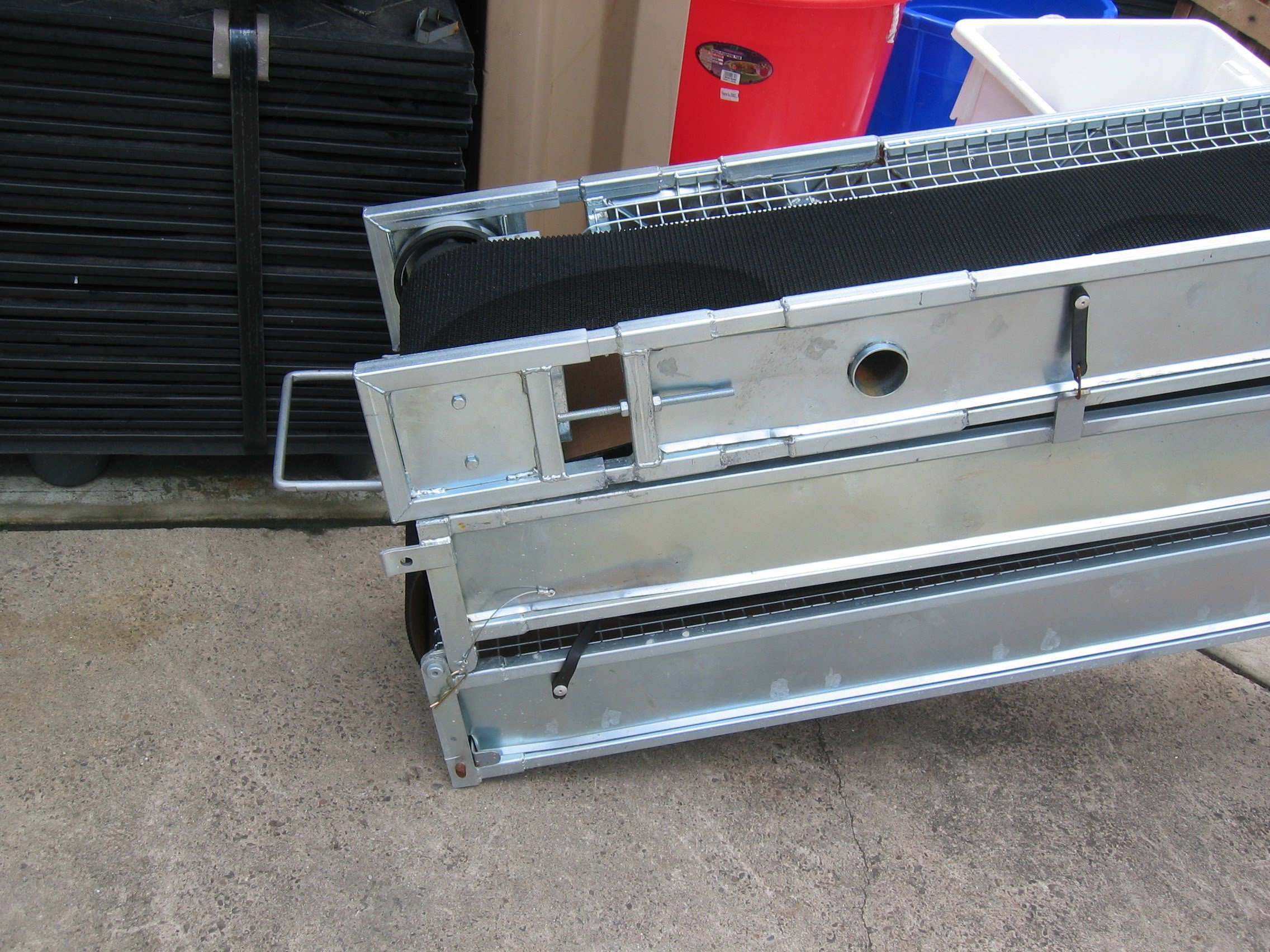 A metal display rack with wheels and multiple shelves, positioned outdoors on a concrete surface.