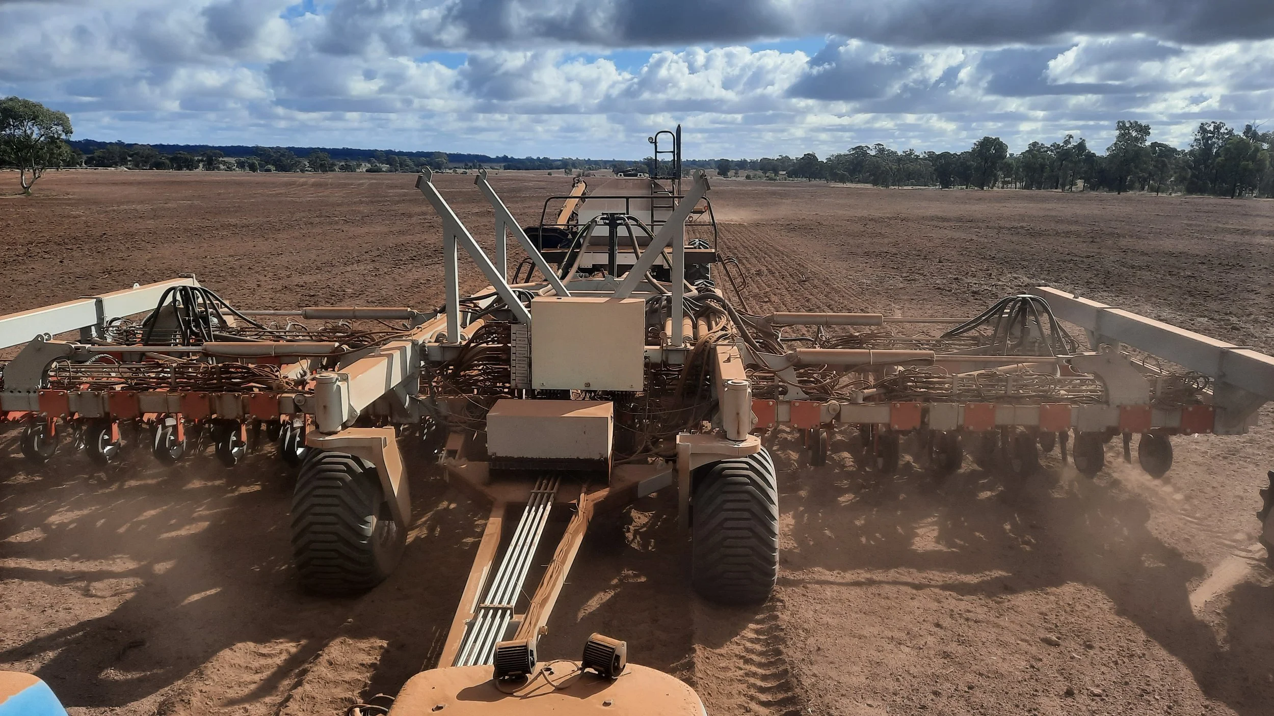 A large agricultural machine in a vast, tilled field under a partly cloudy sky.