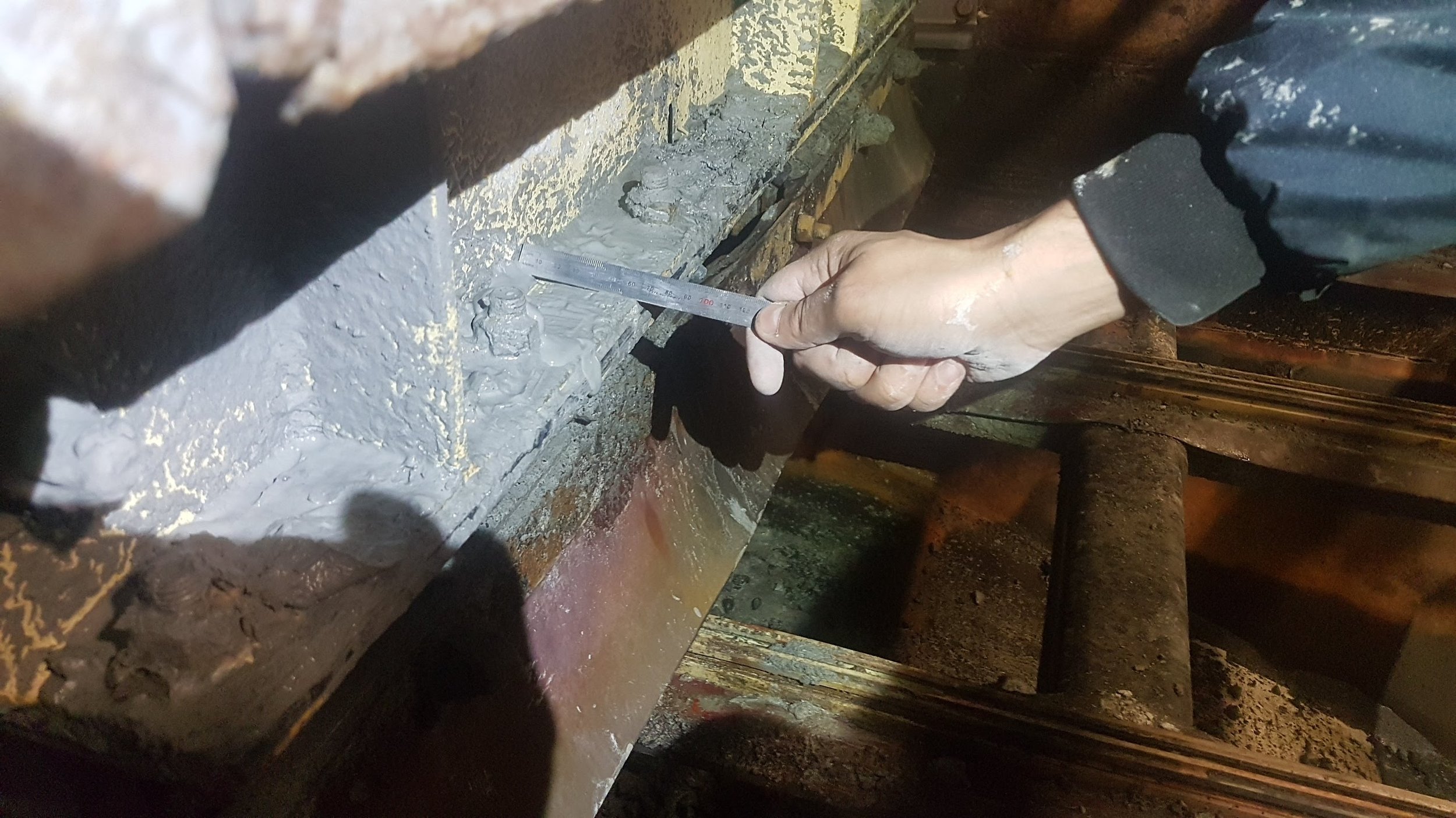 Person measuring a concrete surface with a ruler in a construction or repair setting.