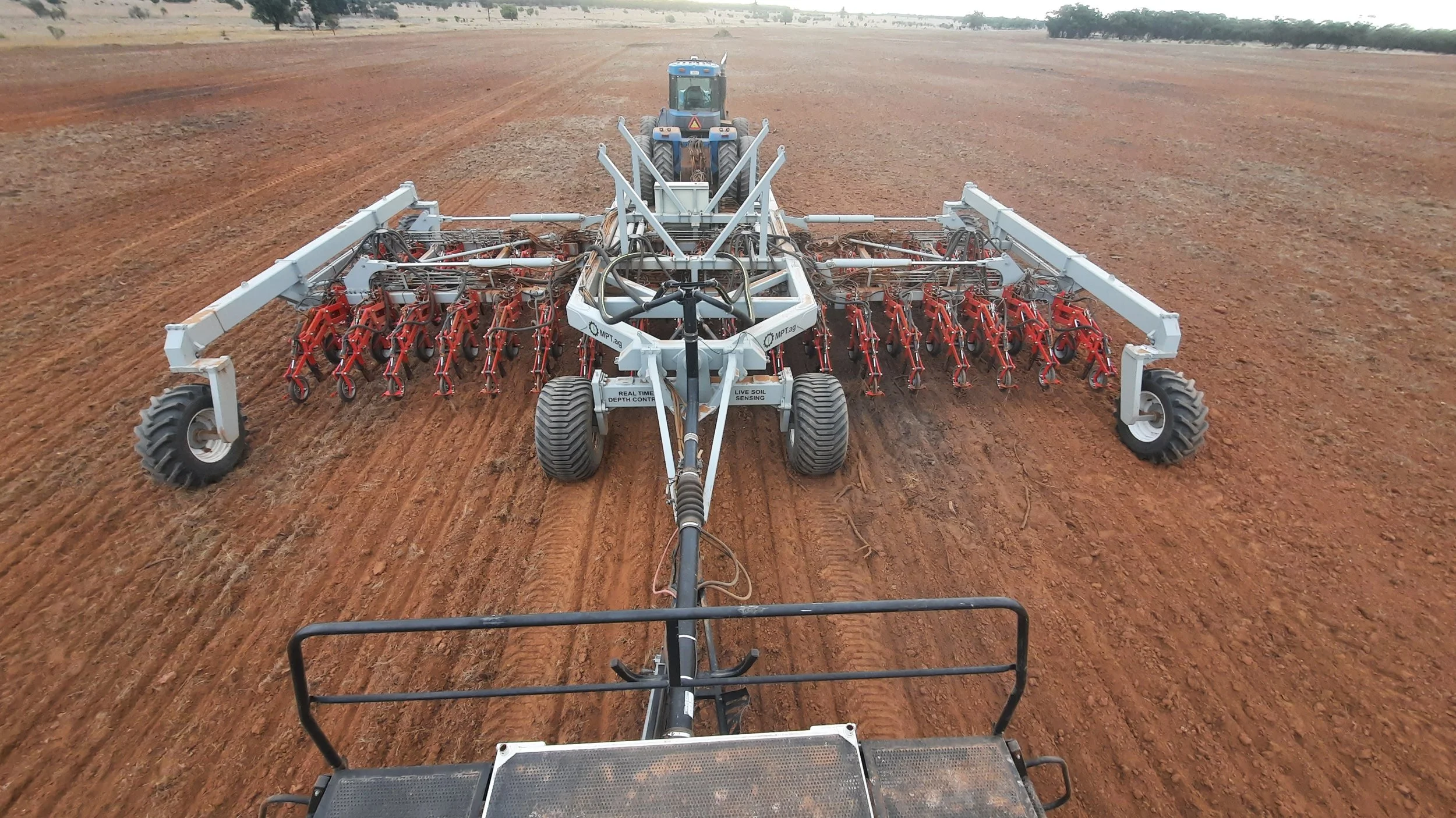 A tractor pulling a large piece of farm equipment, likely a seed drill or planter, across a wide, freshly tilled field during daytime.