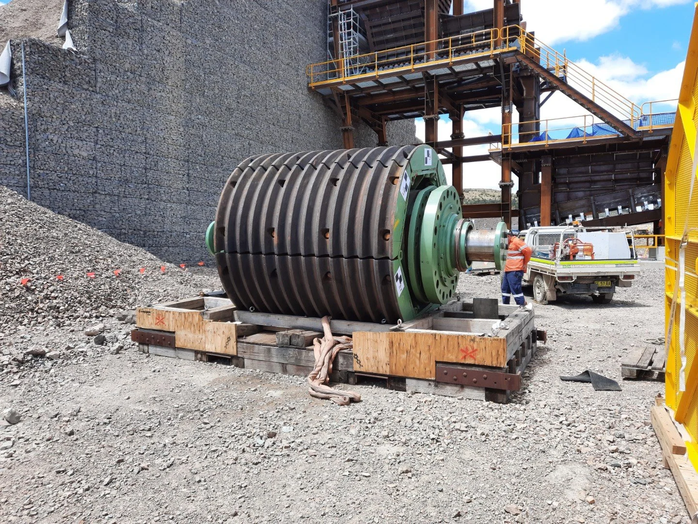 Large industrial grinding or crushing equipment on a construction site with a worker nearby and scaffolding in the background.
