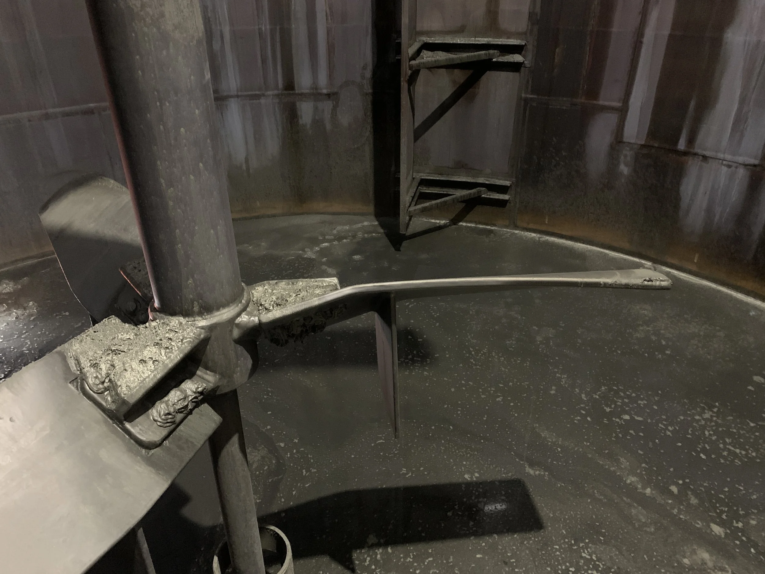 Interior of a large, empty, industrial metal tank with a rusted, rusty staircase attached to the wall inside.