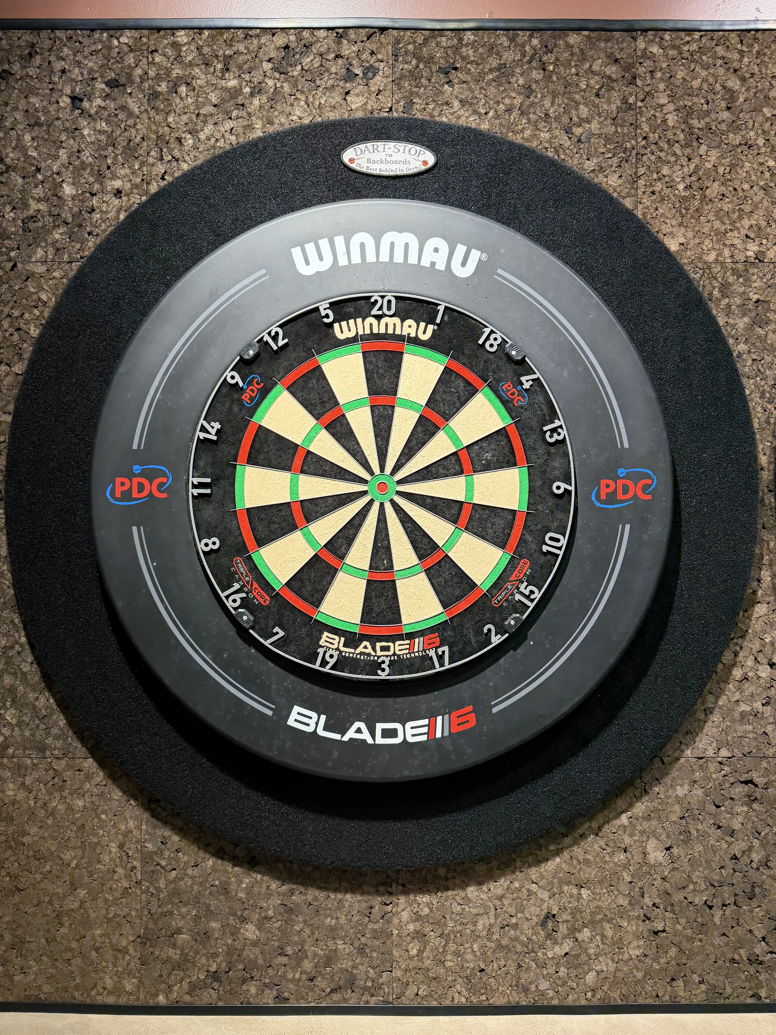 A dartboard with a black, gray, white, red, green, and beige color scheme on a cork-like wall surface.