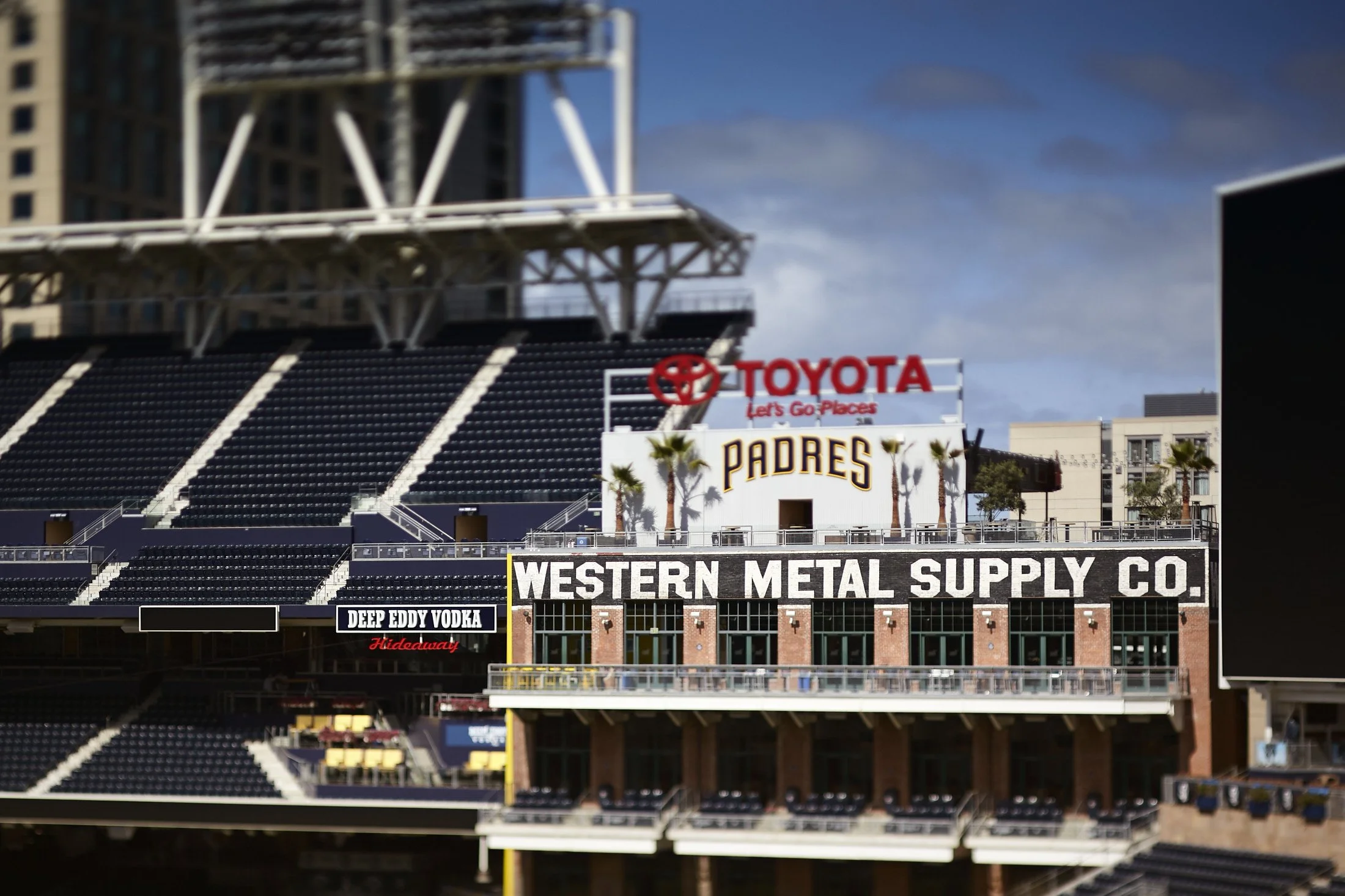 View of Petco Park with signs for Western Metal Supply Co., San Diego Padres, and various advertisements, including Deep Eddy Vodka, under a partly cloudy sky.