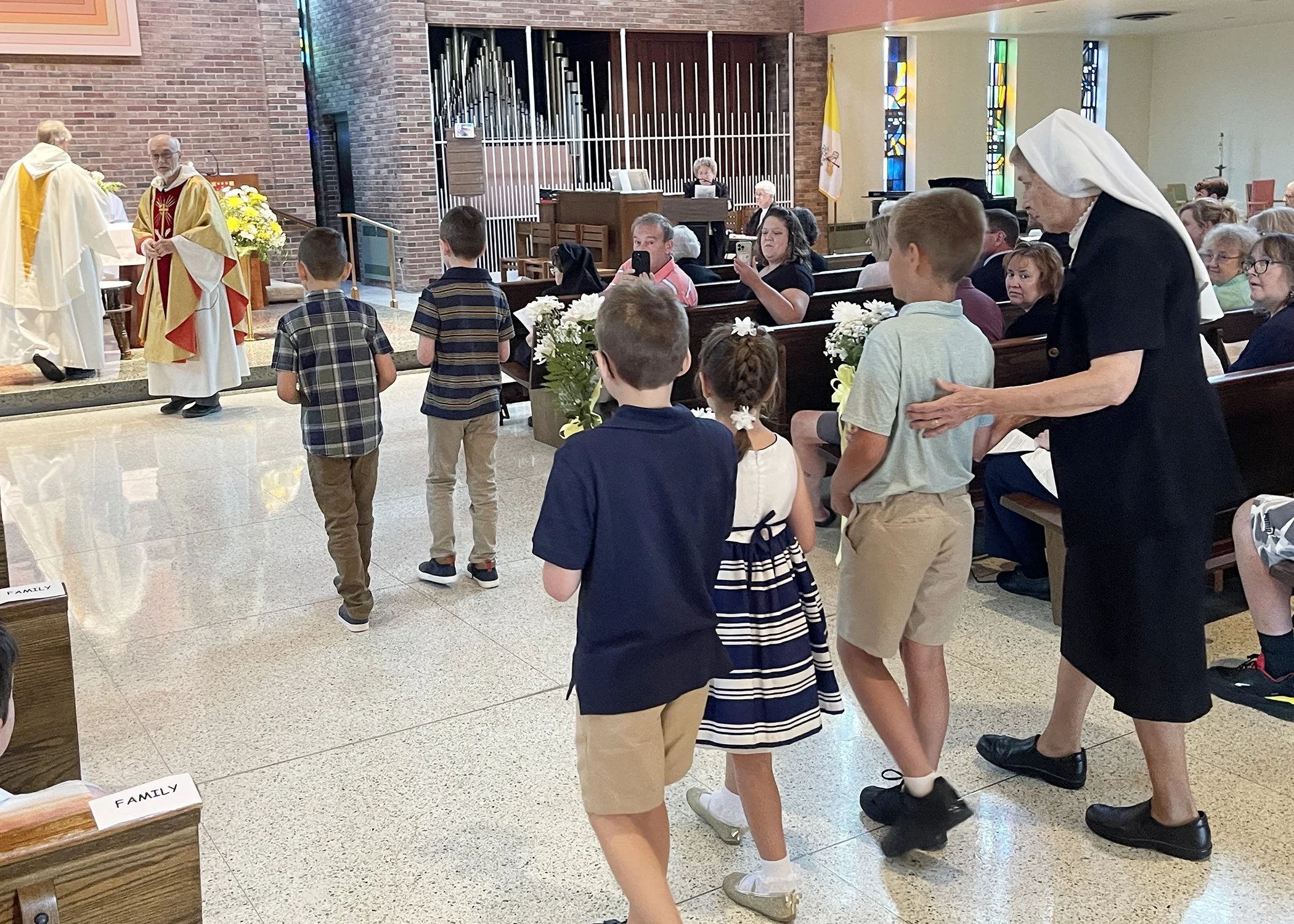  Sister Kevin Berdis guides young members of the Jacko Family in the offertory procession during Sister Cecilia Jacko's 75th Jubilee Mass on July 13, 2024. 