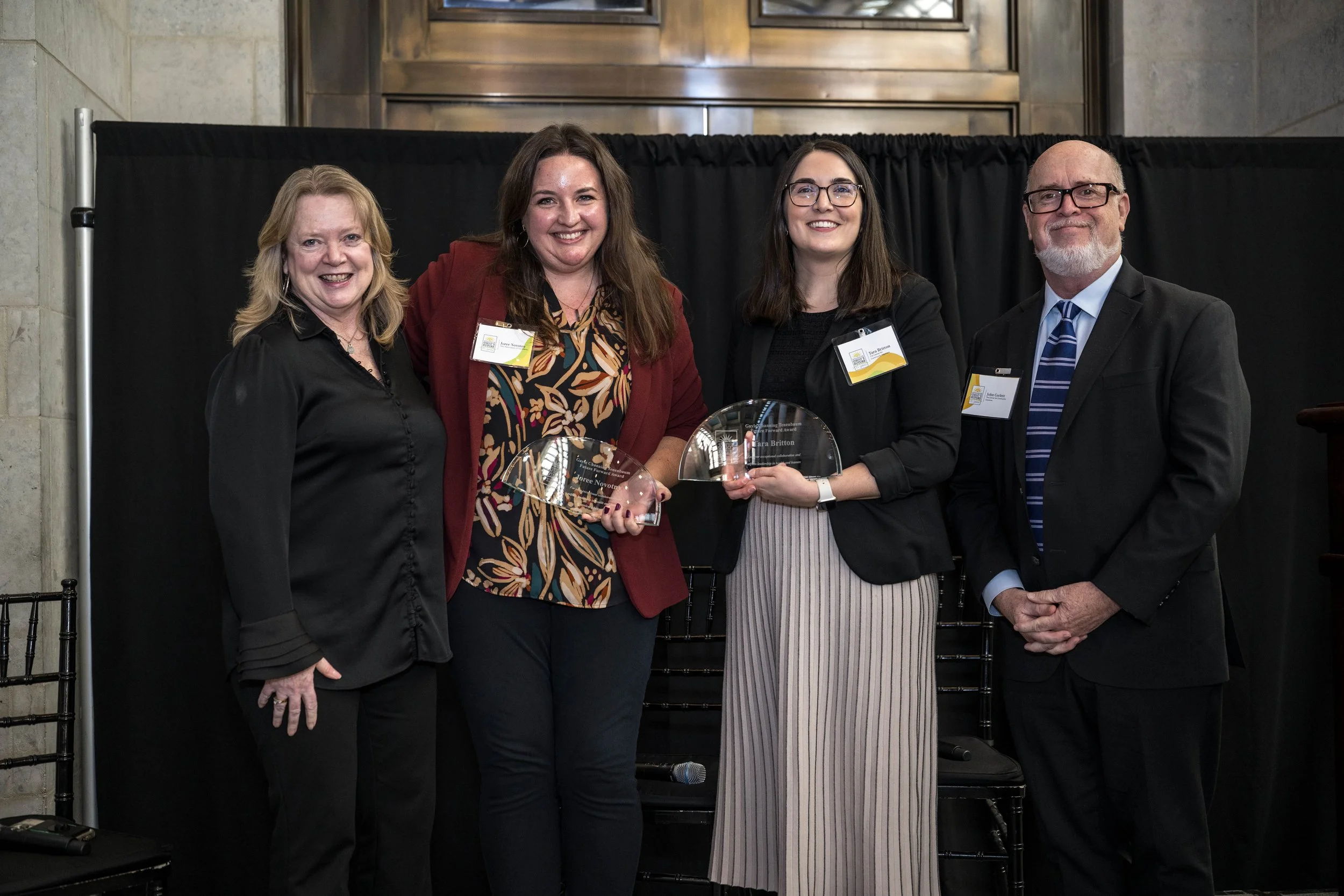  Marcia Egbert, Joree Novotny, Tara Britton, and John Corlett posing after their fireside conversation onstage. Joree Novotny and Tara Britton were the recipients of the inaugural Gayle Channing Tenenbaum Future Forward Award to recognize outstanding