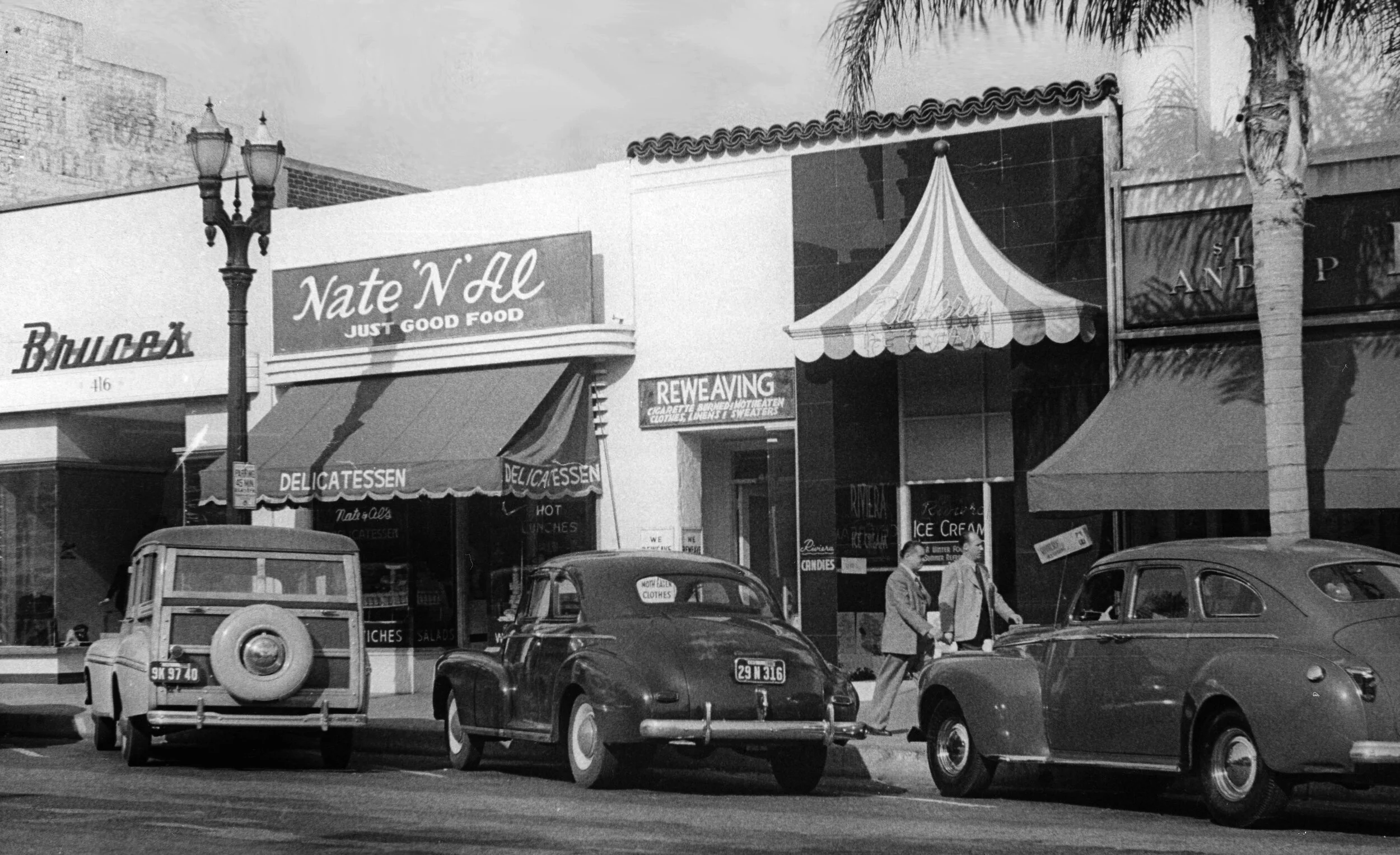 Vintage, 1940’s era exterior photograph of Nate ‘N’ Al, “Just Good Food,” delicatessen, with vintage cars parked outside.