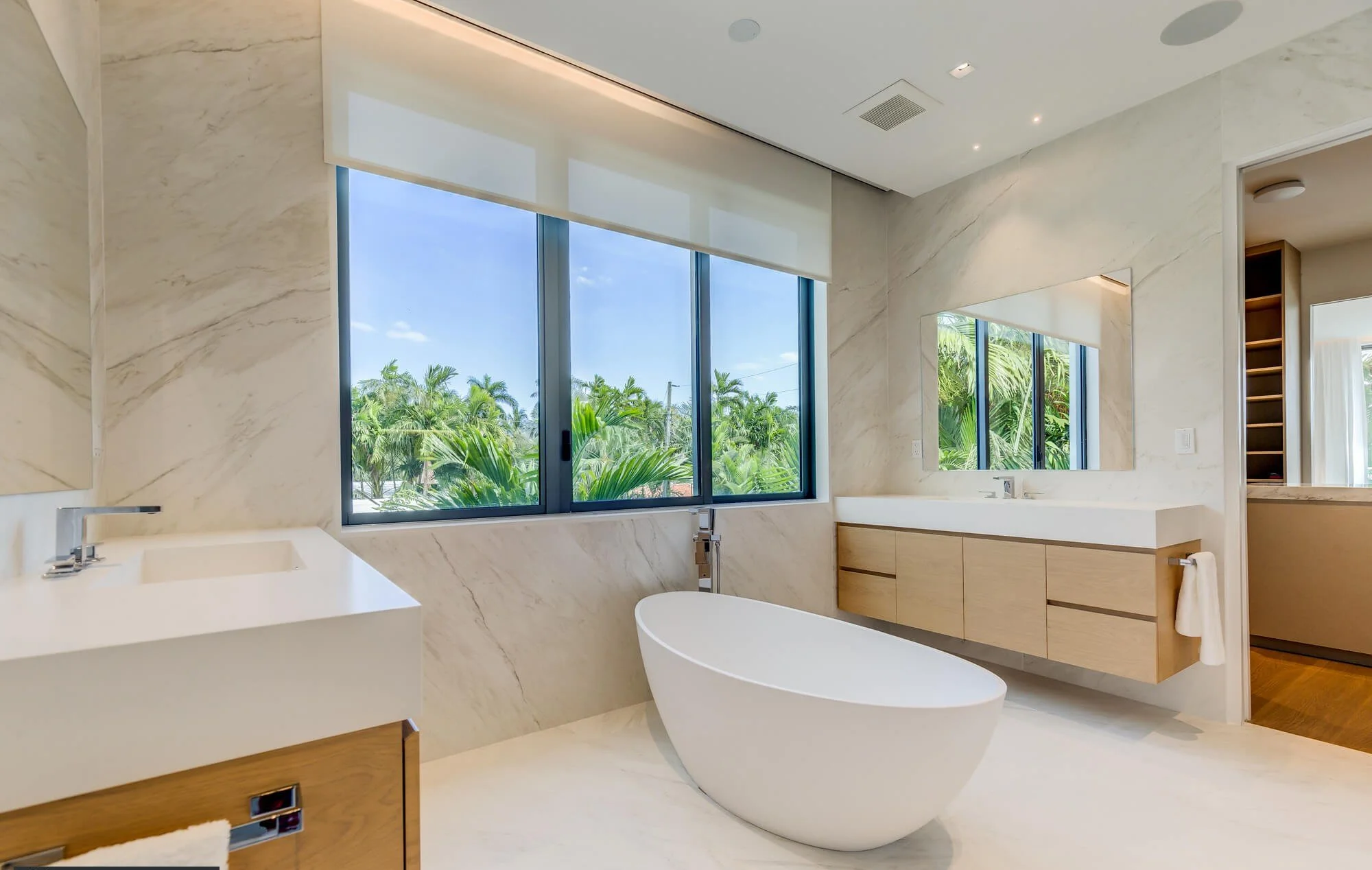 a calming bathroom of neutral tones. marble clad walls and floors and central ceramic tub.