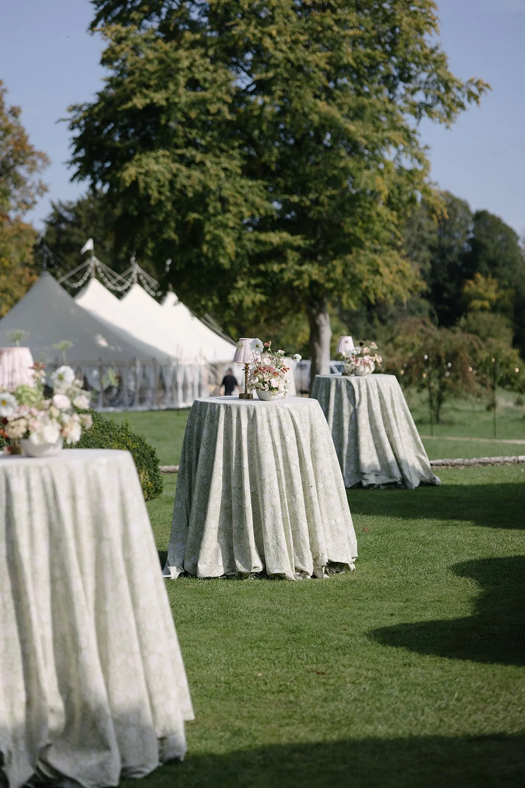 Outdoor wedding reception tables at Cornwell Manor with seasonal garden-style floral centrepieces beneath a sailcloth marquee, styled with bespoke luxury wedding flowers by The Botany House in collaboration with Attabara Studio.