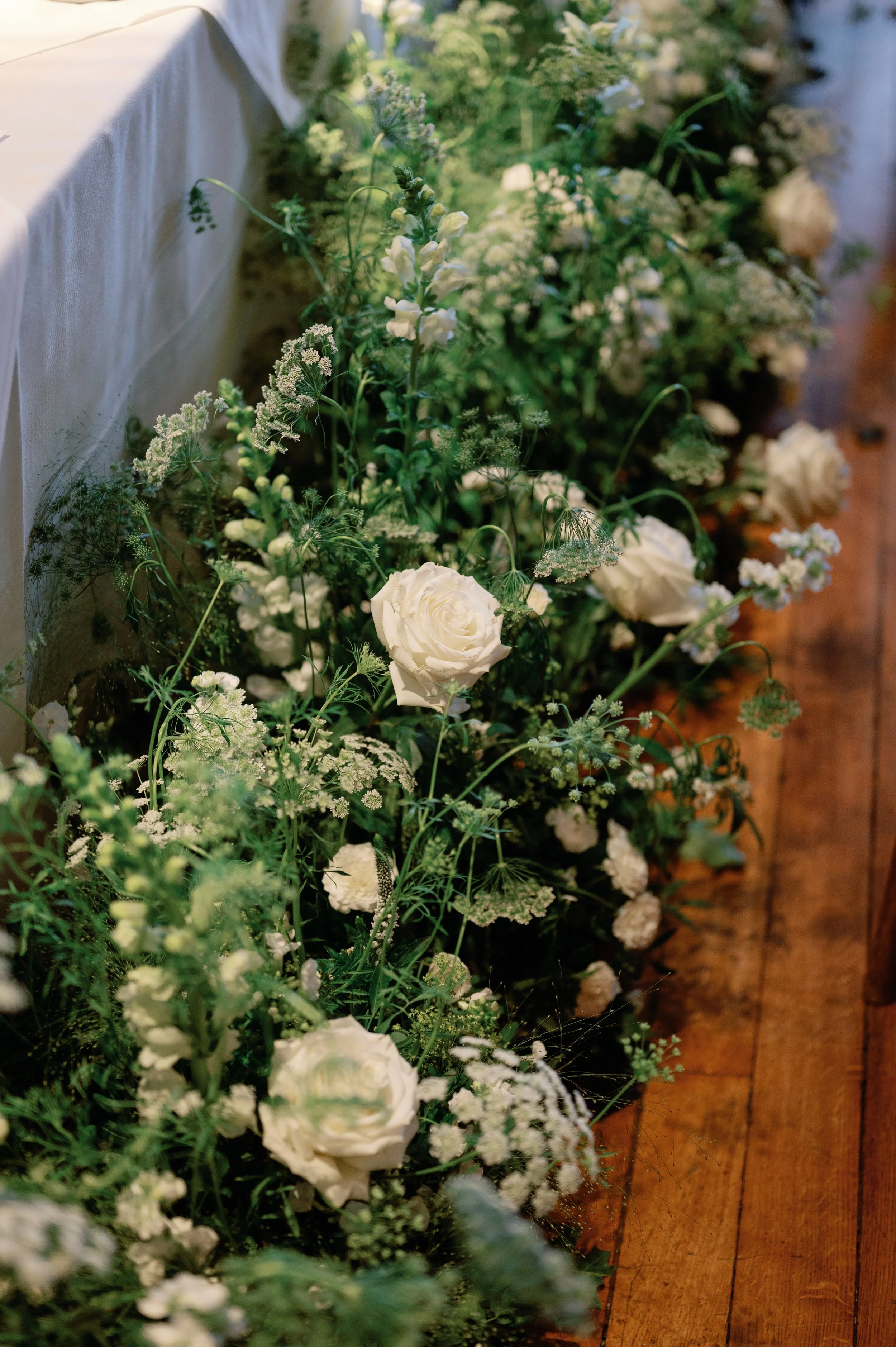 White floral arrangement with roses and other greenery on a wooden floor.