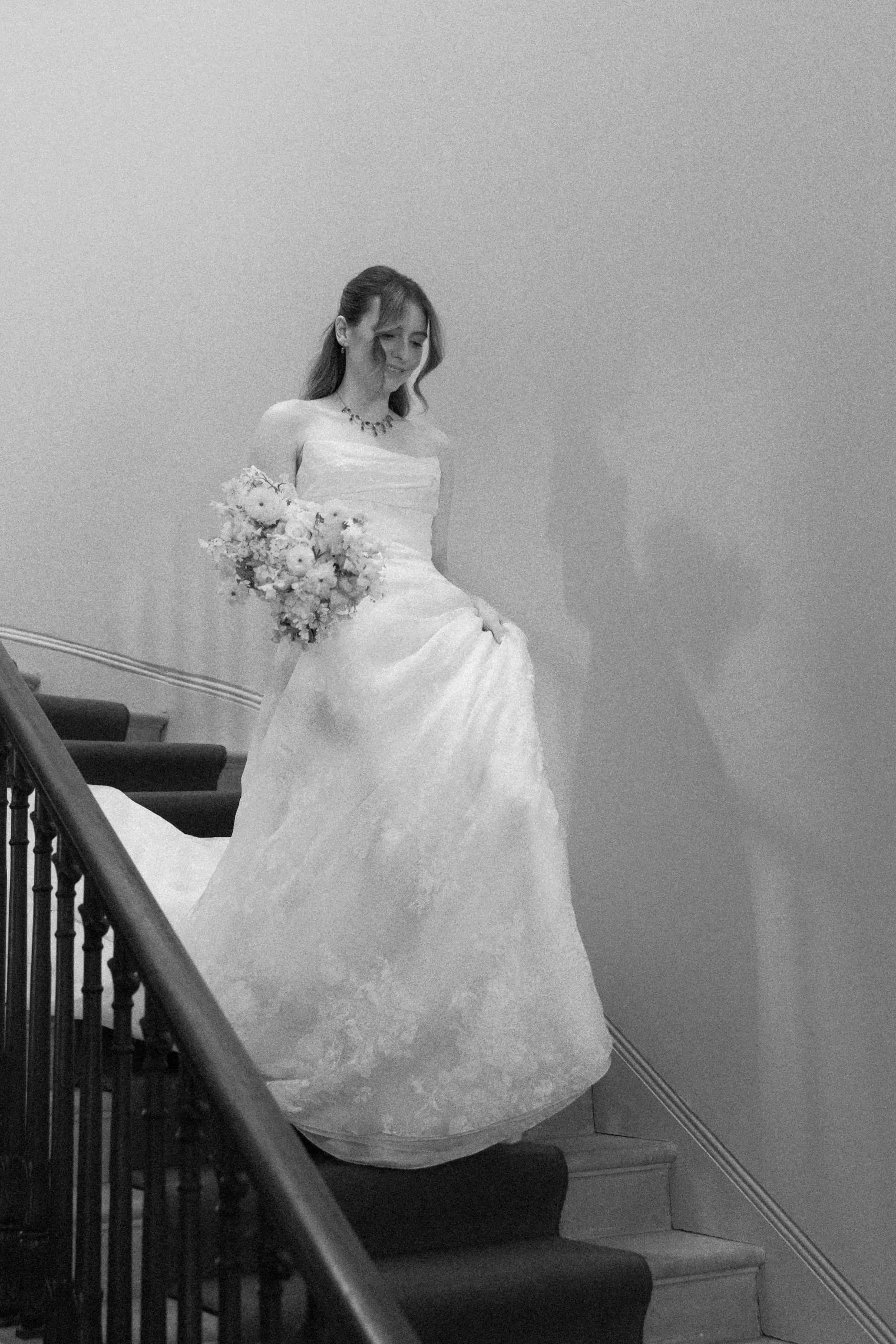 A bride in a wedding dress holding a bouquet of flowers walking down stairs. Wilderness Reserve, Suffolk, The Botany House Florist