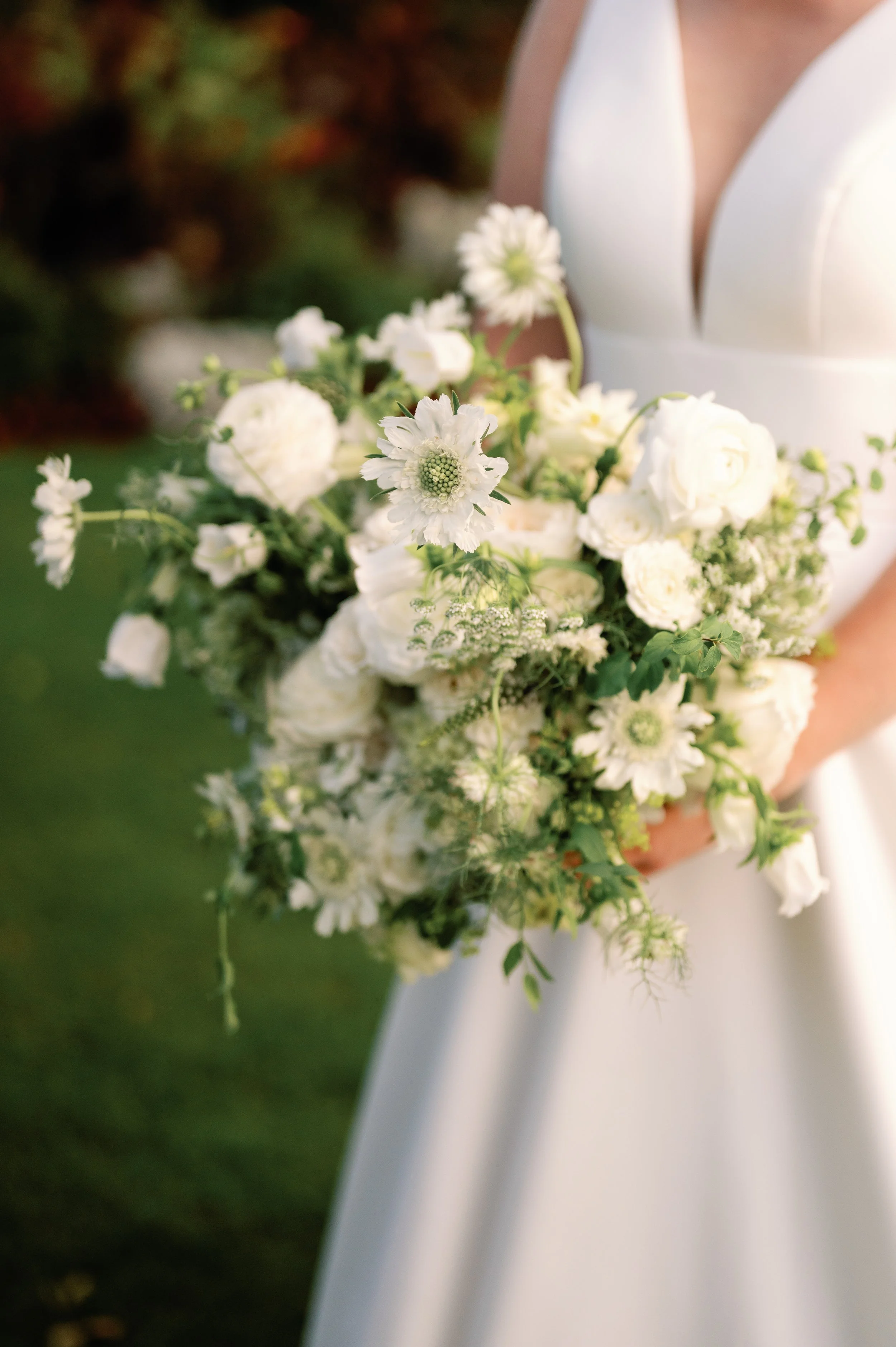 A bride holding a bouquet of white flowers, including roses, daisies, and greenery, wearing a white wedding dress.