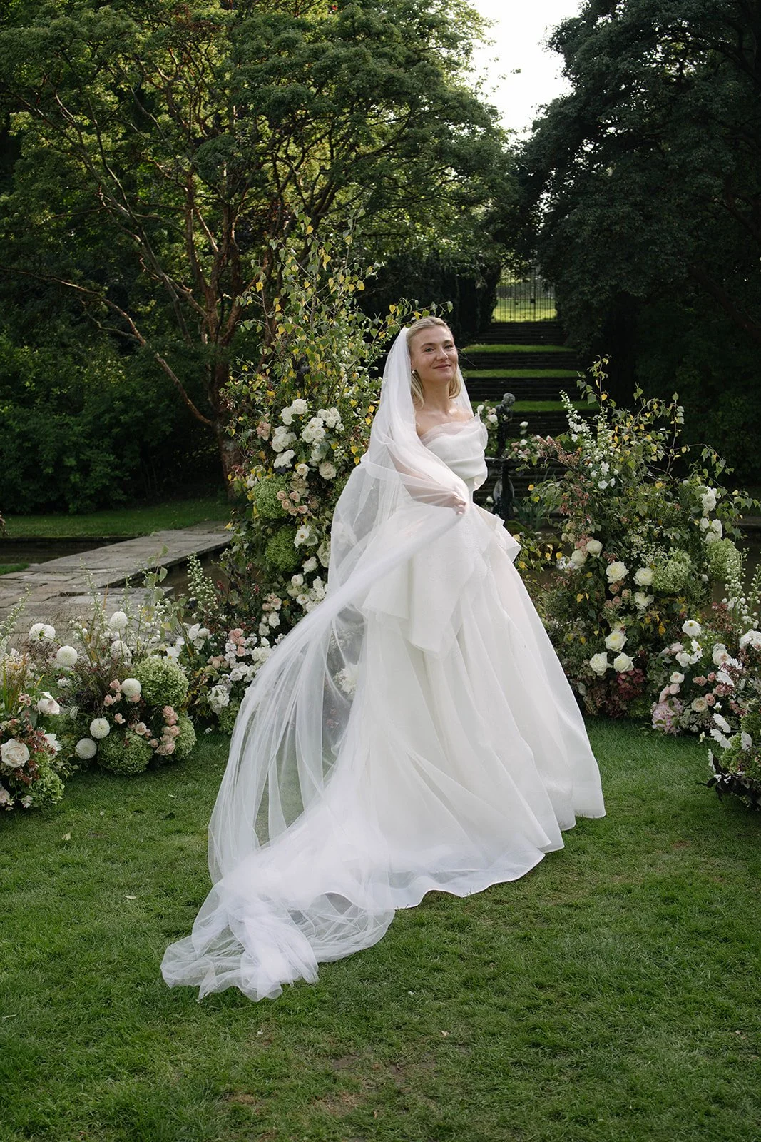 Bride in a white wedding dress and veil at a Cornwell Manor wedding, surrounded by luxury garden-style floral arrangements by The Botany House wedding florist.