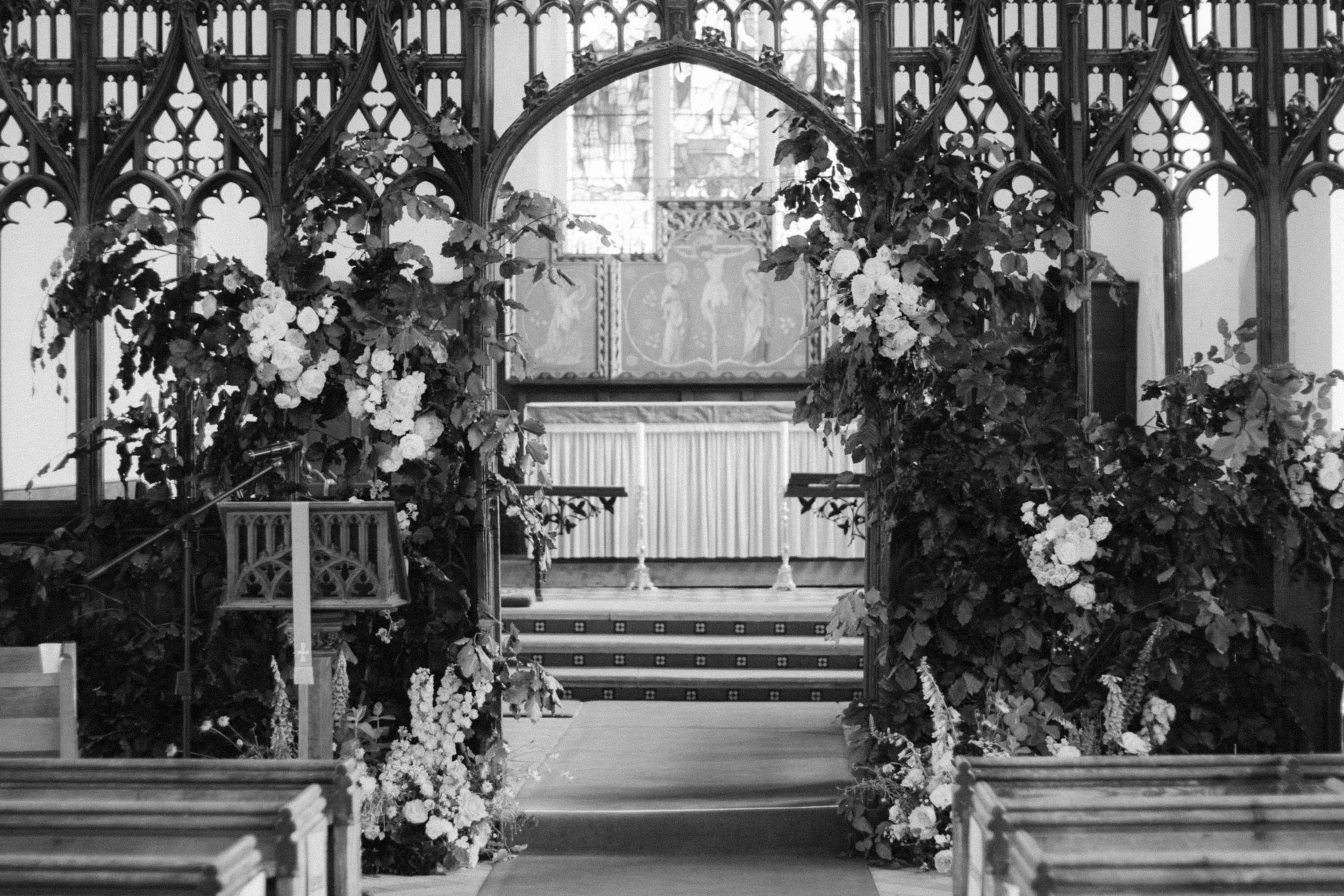 A floral archway decorated with flowers leading up to an altar in a church, with wooden pews on either side.