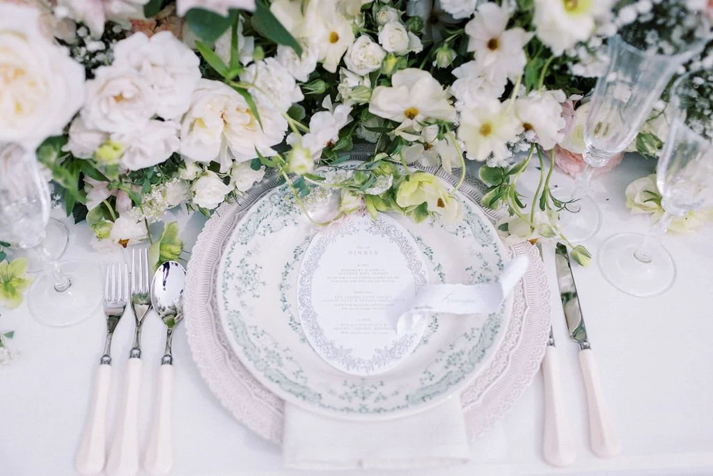 Elegant table setting with floral centerpiece, decorative plates, wine glasses, and cutlery on a white tablecloth.