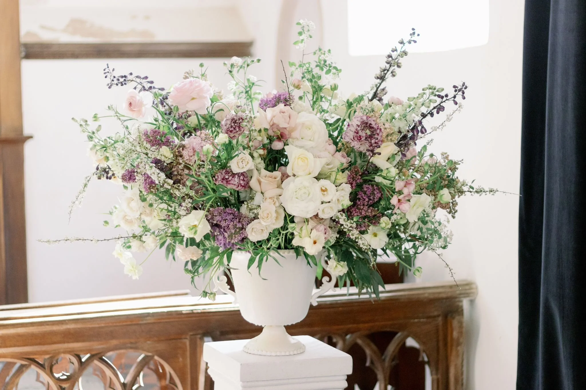 Elegant floral arrangement with white, pink, and purple flowers in a white vase on a wooden table.