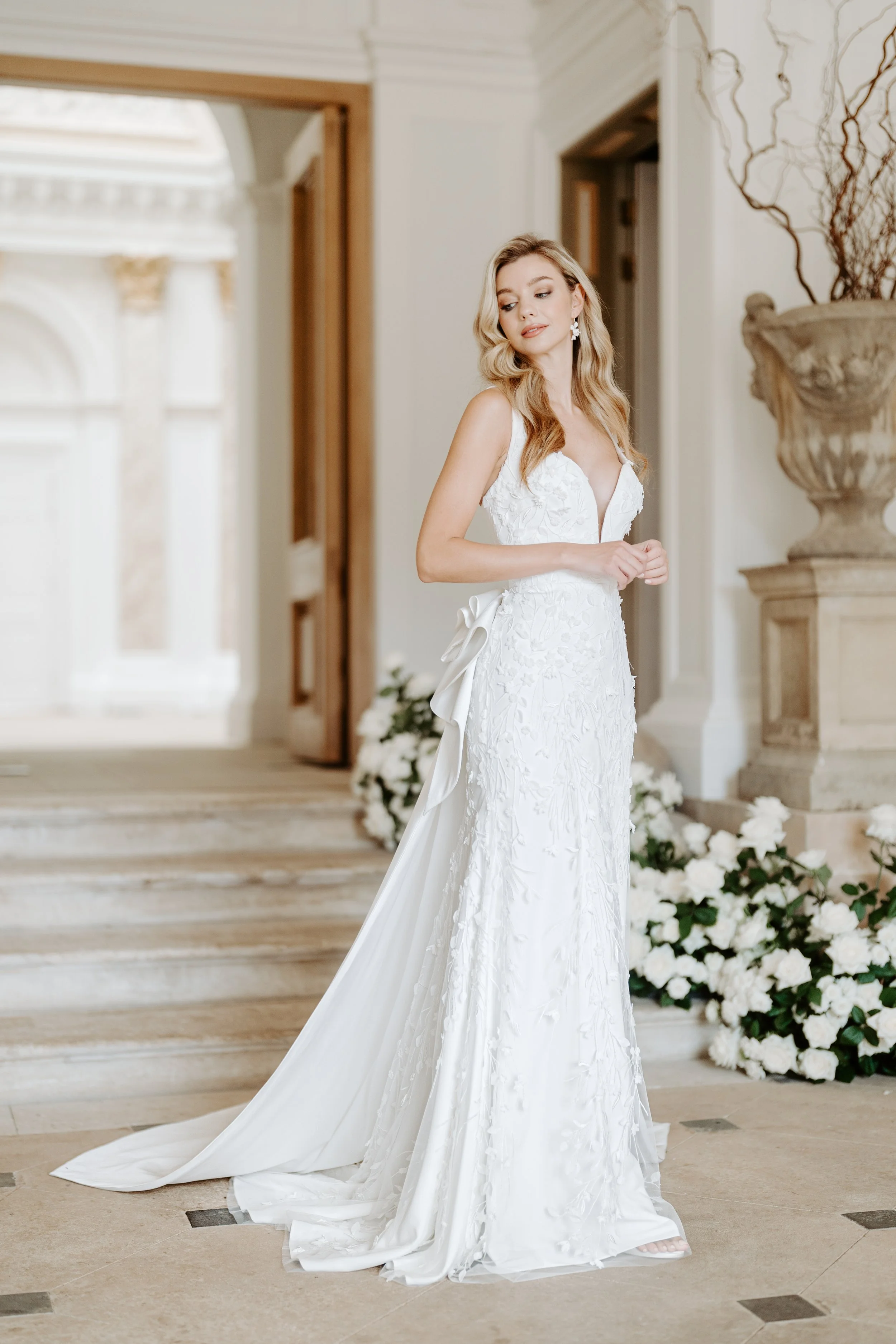 A woman in a white wedding dress standing in an elegant indoor setting decorated with white flowers.