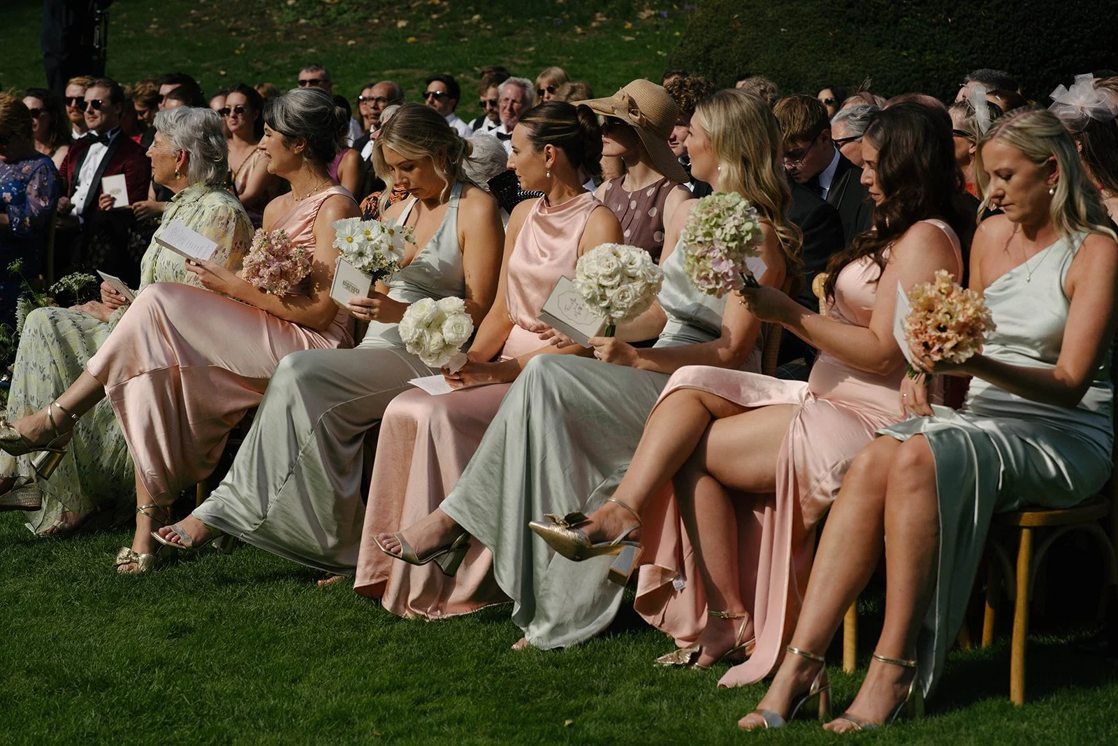 Bridesmaids in pastel dresses holding blush and cream bouquets at a Cornwell Manor outdoor wedding, styled with bespoke luxury wedding flowers by The Botany House wedding florist.