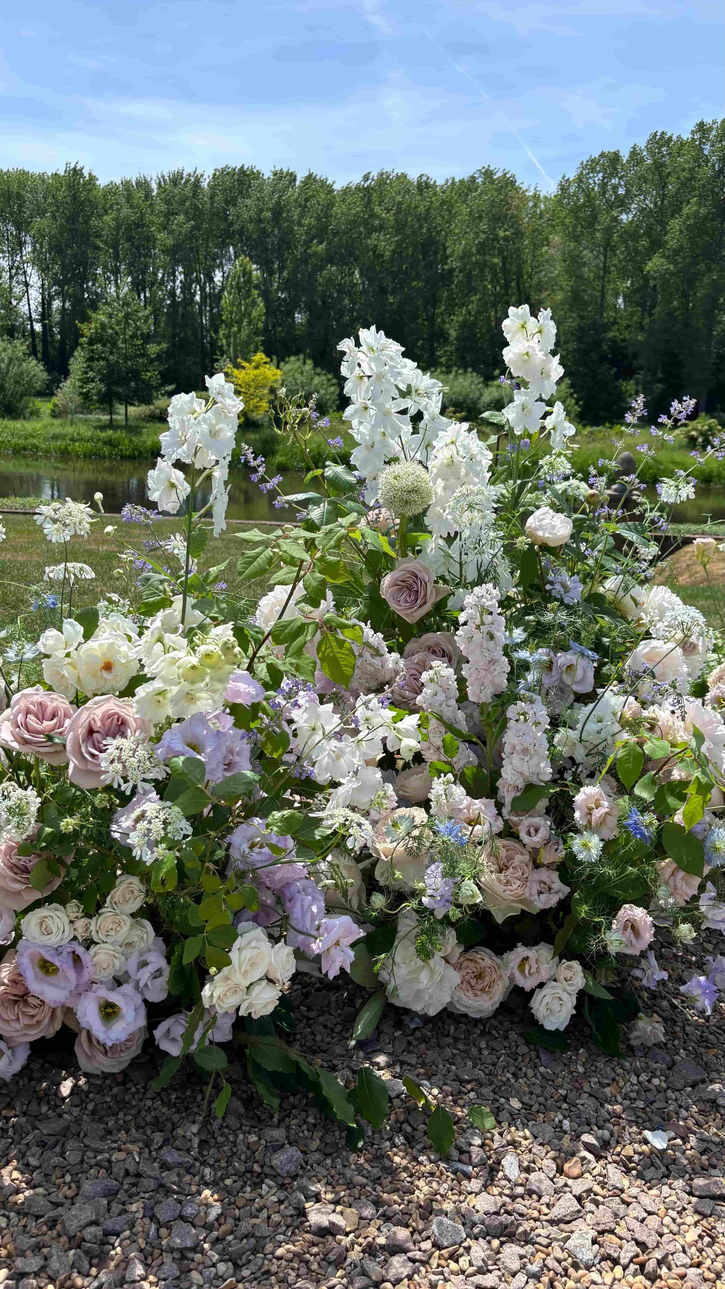 Romantic lakeside wedding flower installation with soft lilac, blush and white seasonal flowers at Oxnard Hall