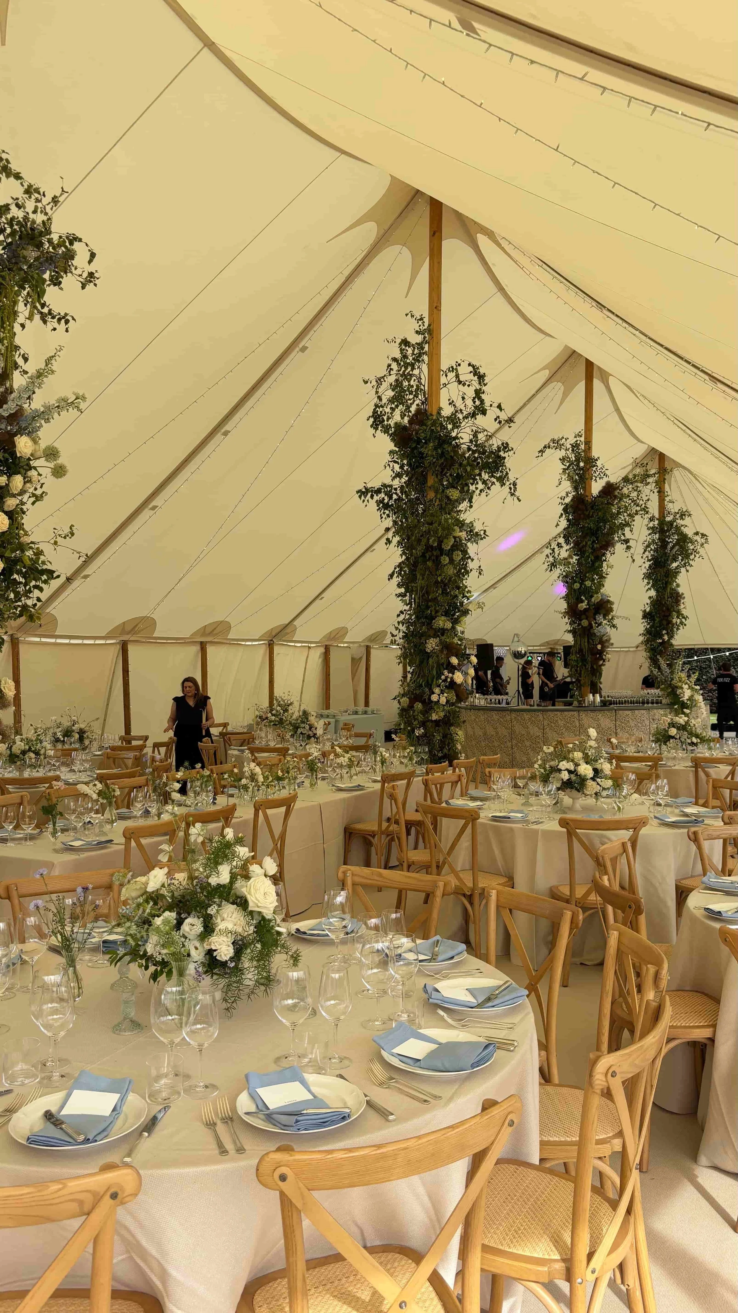 Elegant marquee wedding reception with garden-style table flowers and climbing greenery around the tent poles