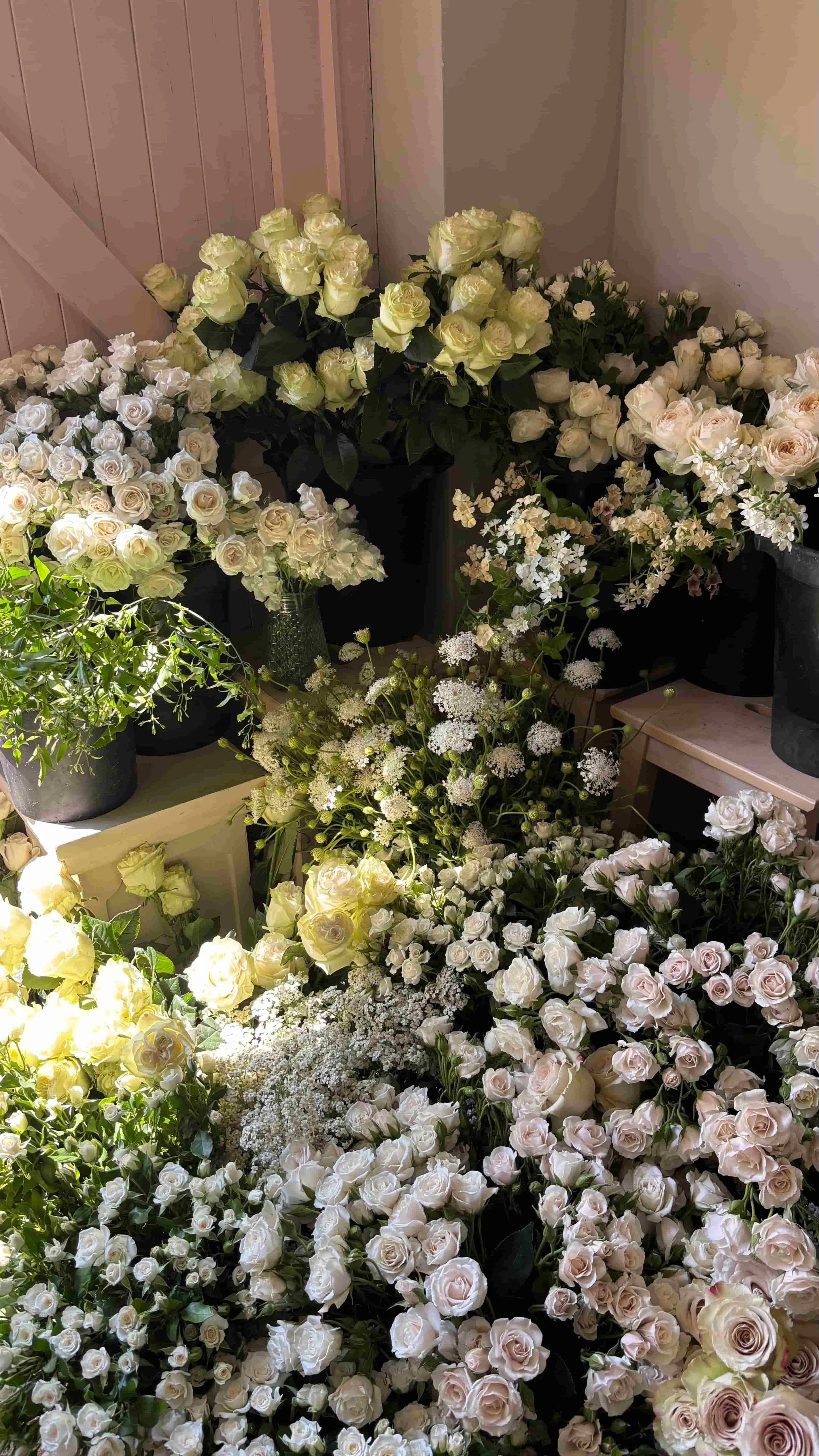 Buckets of white and blush seasonal wedding flowers including roses, lace flowers and soft greenery ready for arranging