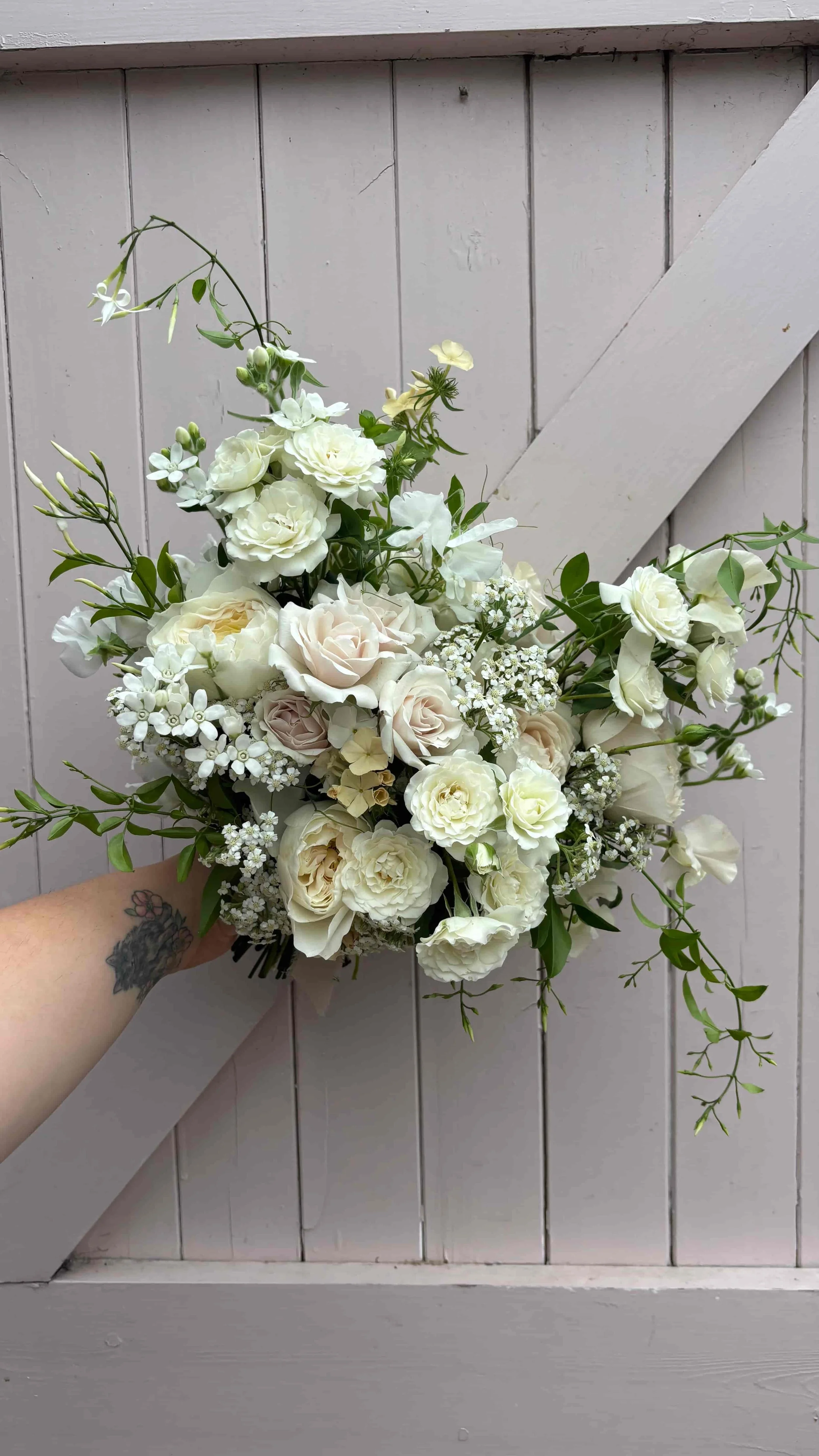 Romantic garden-style bridal bouquet with white and blush roses, delicate seasonal flowers and trailing greenery