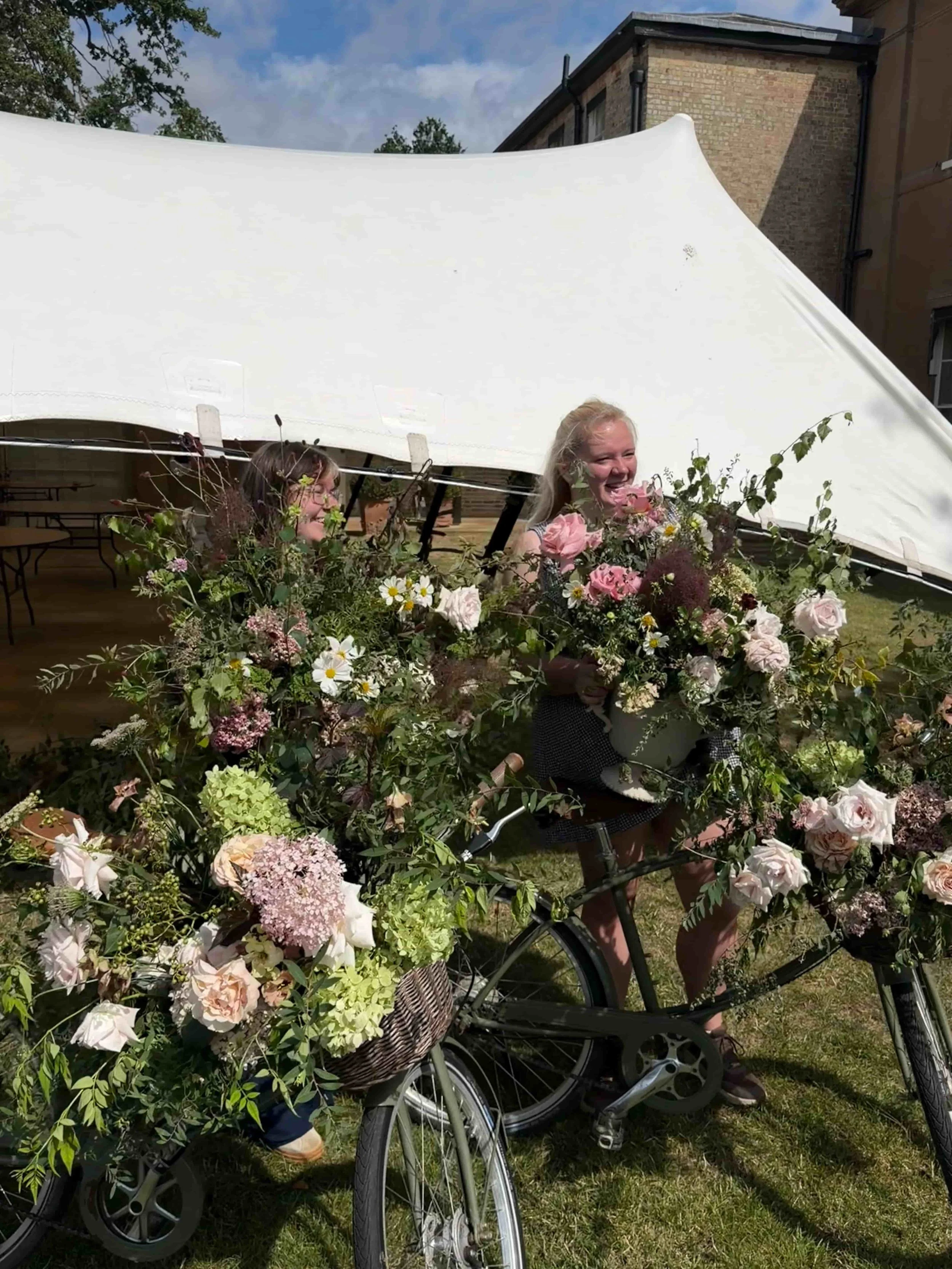 The Botany House floral team carrying large garden-style wedding arrangements during a summer marquee installation at Wilderness Reserve