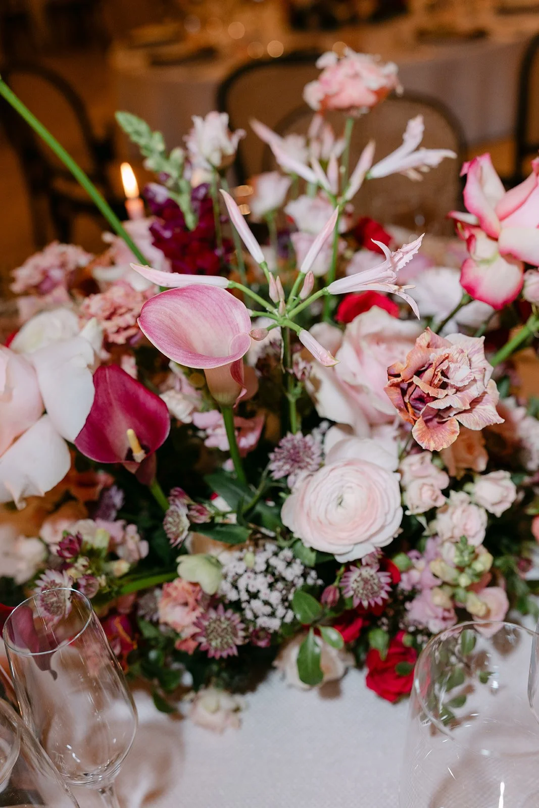 Close-up of a floral centerpiece with pink, white, and red flowers on a table with wine glasses in the foreground.