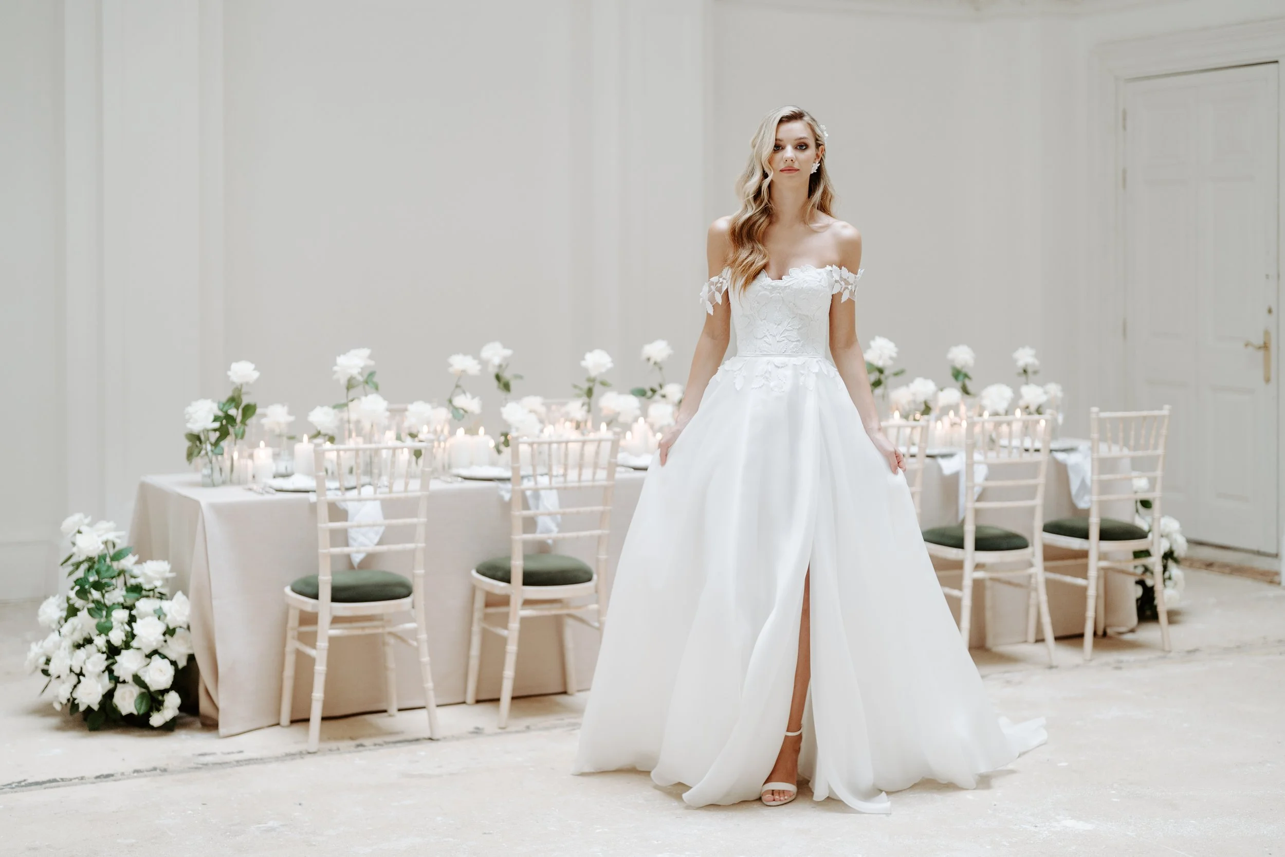 A woman in a white wedding dress standing in a decorated banquet hall with a long table set for a wedding reception.