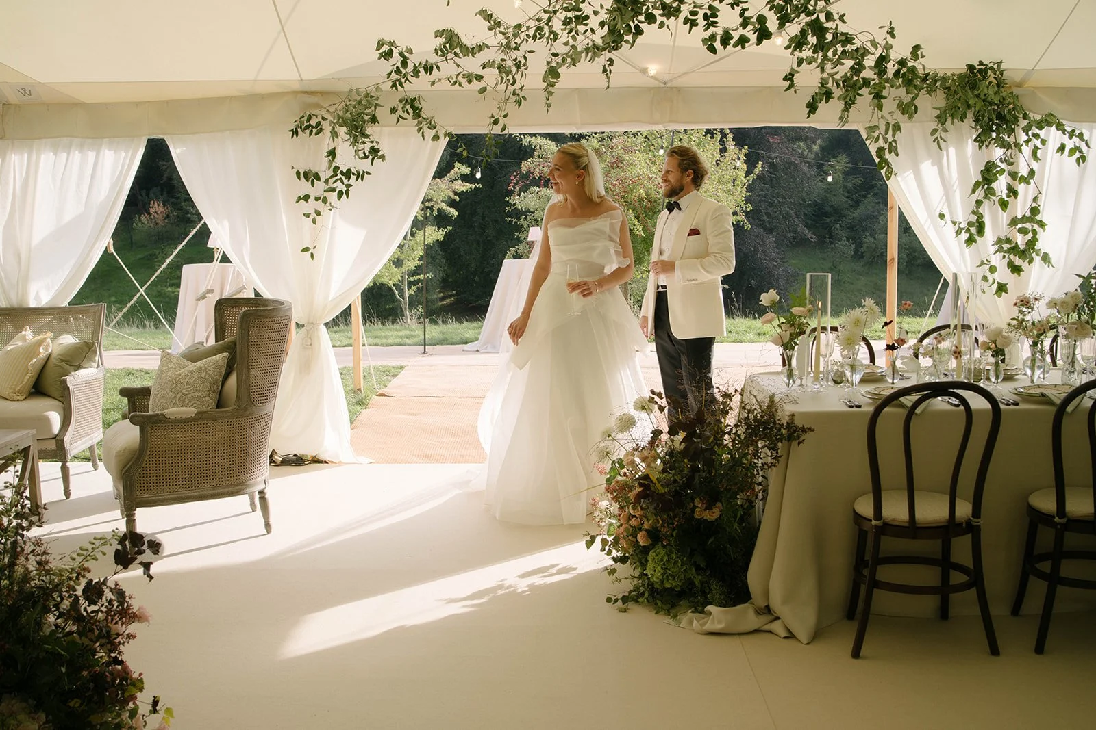 Newlyweds during an outdoor ceremony at Cornwell Manor holding champagne beneath trees and festoon lights styled with luxury garden style floristry by The Botany House