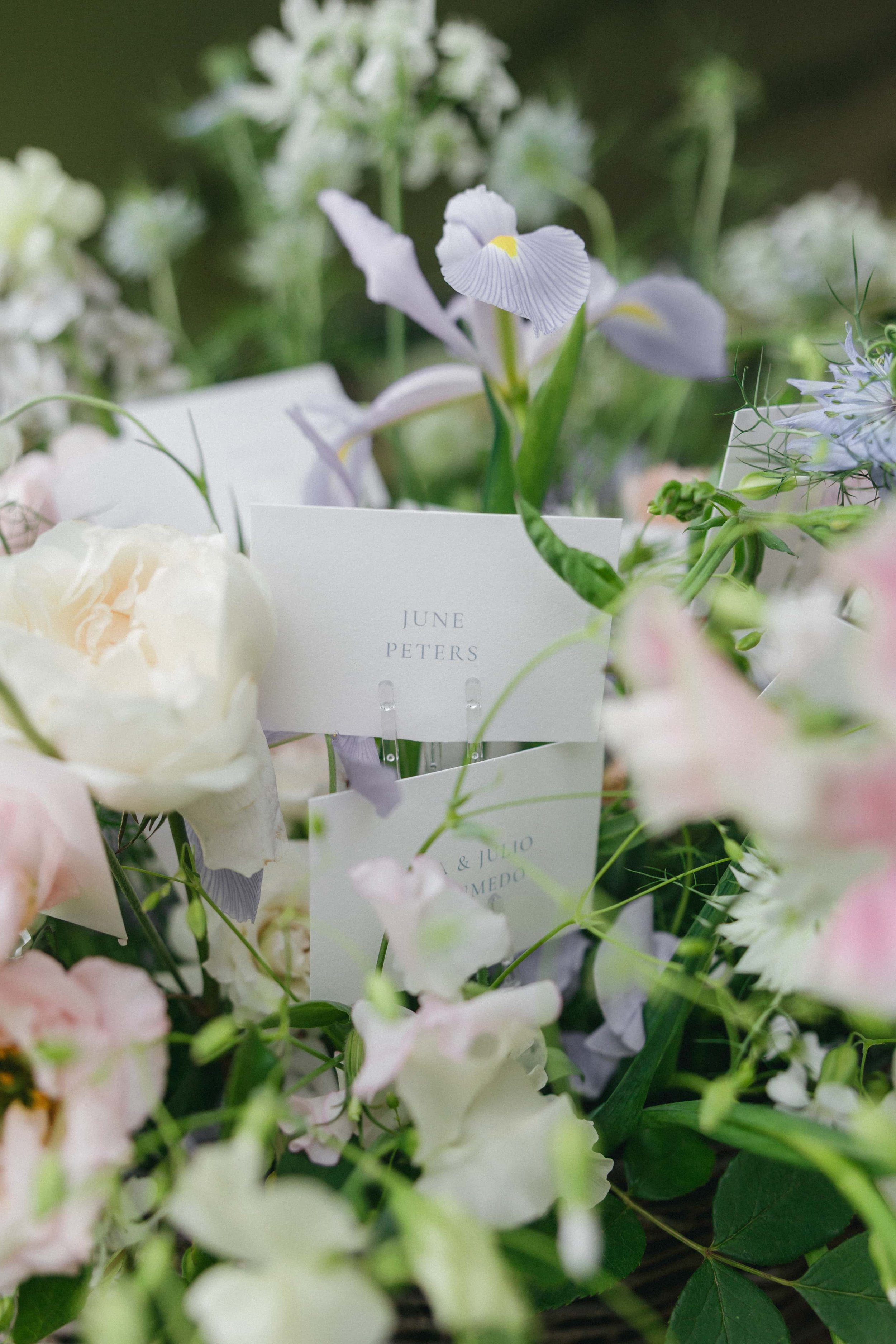 Close-up of a floral arrangement with white and pastel pink flowers, including an iris, with a white card reading 'June Peters' among the blooms. Wilderness Reserve, Suffolk Florals By The Botany House